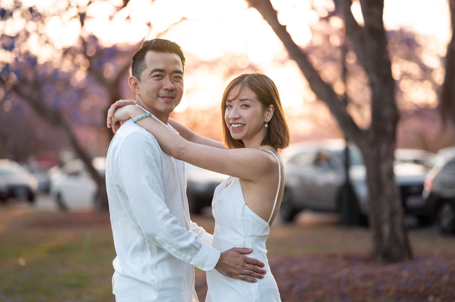 Happy couple in white attire sharing romantic moment at sunset.
