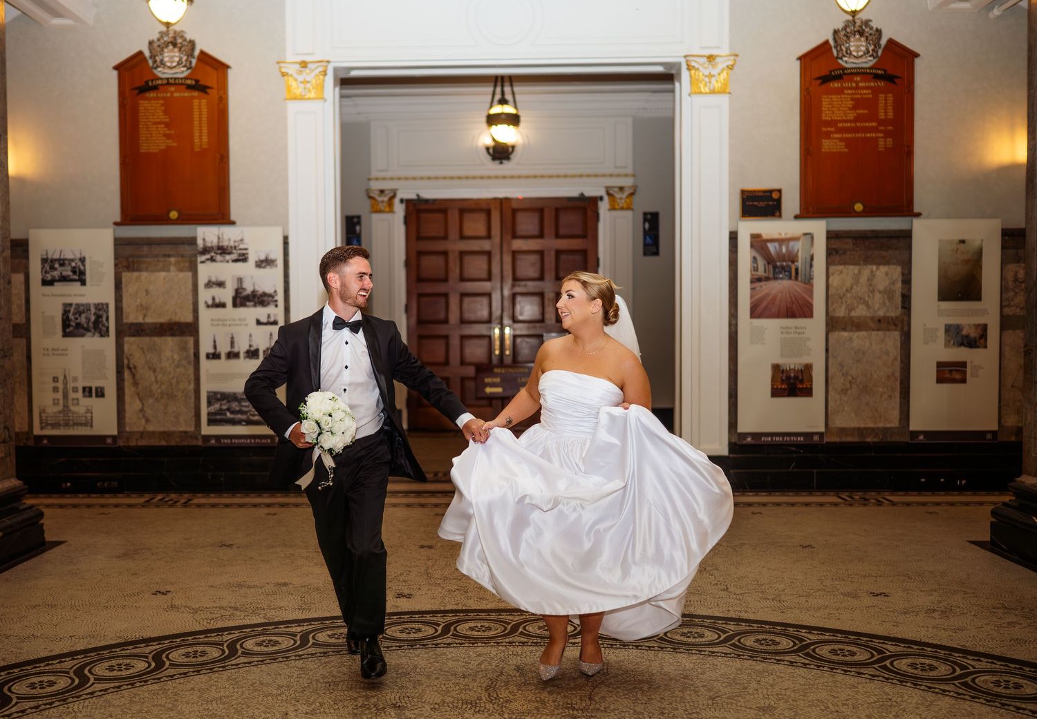 Wedding couple dances together in an elegant ballroom with wood paneled walls and warm lighting.
