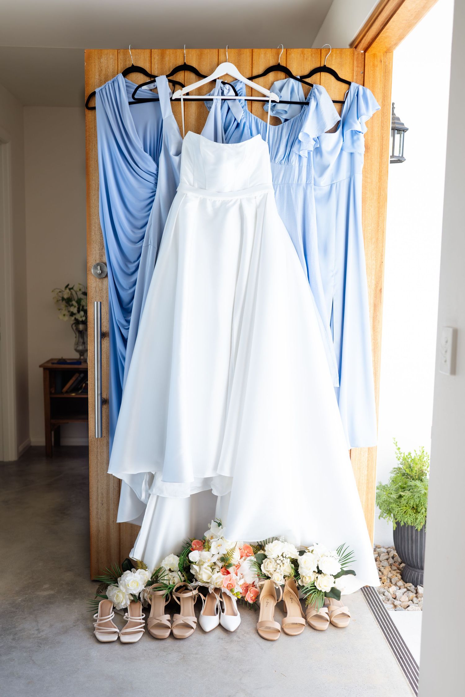 White wedding gown and blue bridesmaid dresses hanging with heels and bouquets below.