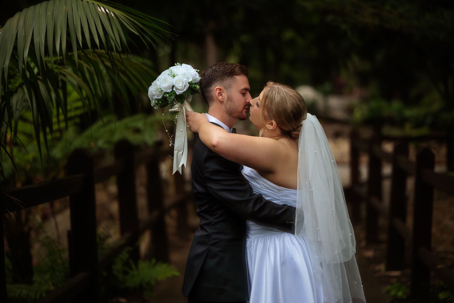Newlywed couple shares romantic kisses in a garden setting during their wedding photo session.