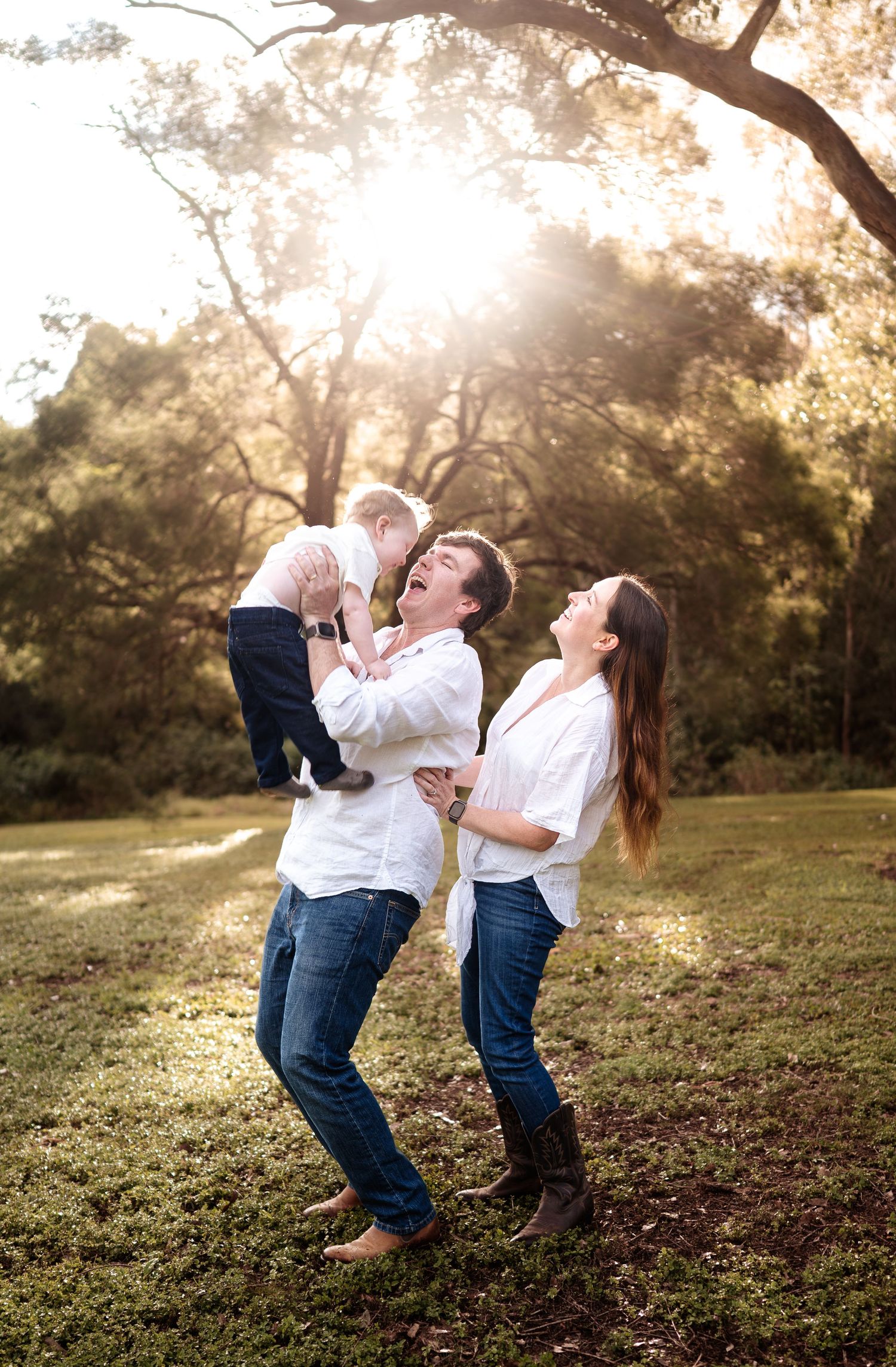 Playful family interaction under a large tree branch during sunset.