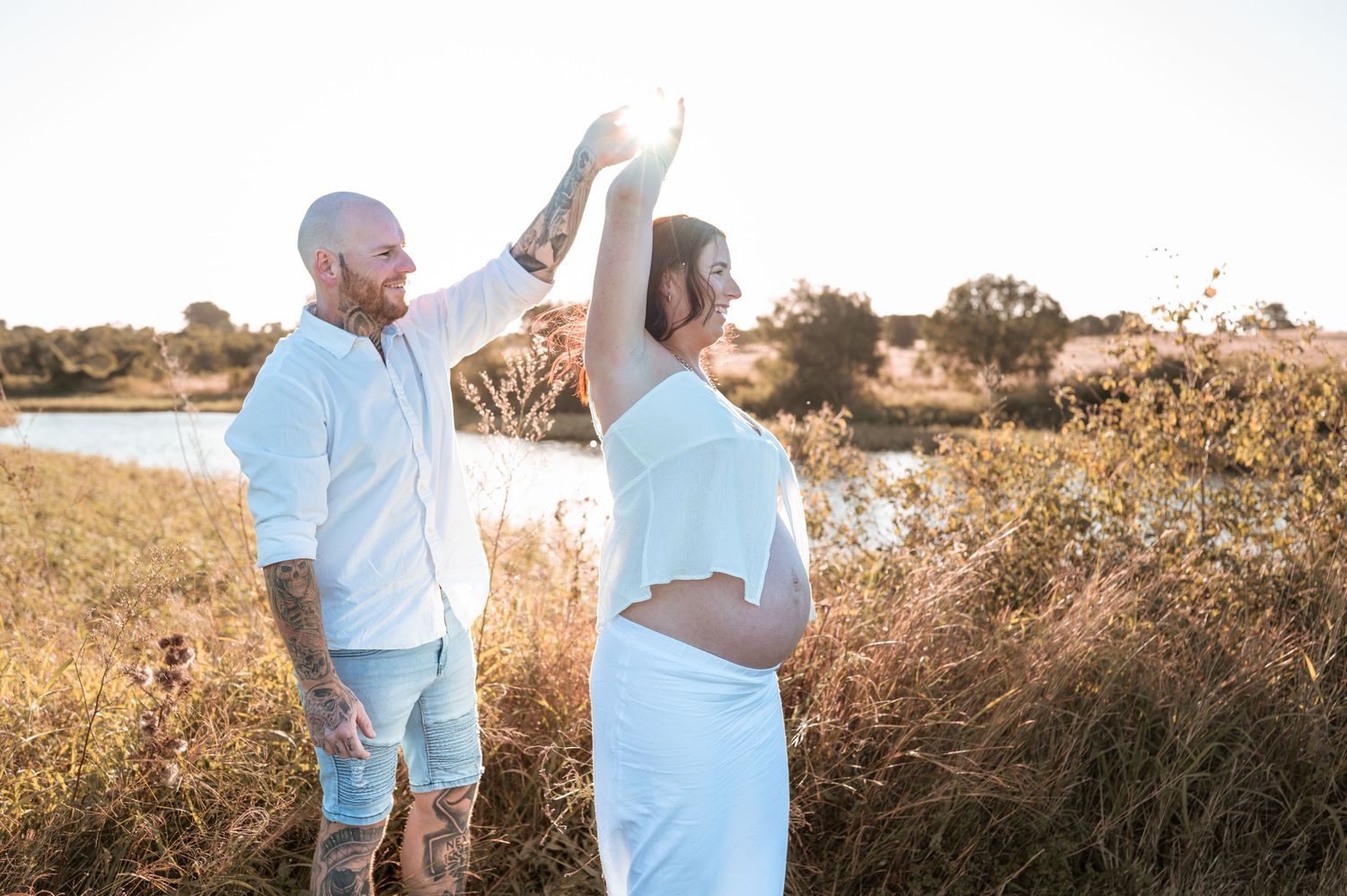 Couple embracing during outdoor maternity photoshoot in golden sunlight.