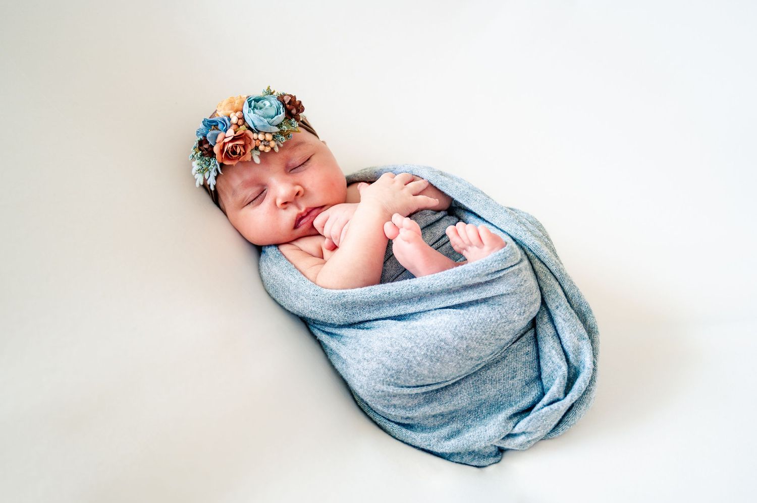 Sleeping newborn wrapped in blue blanket on white background.