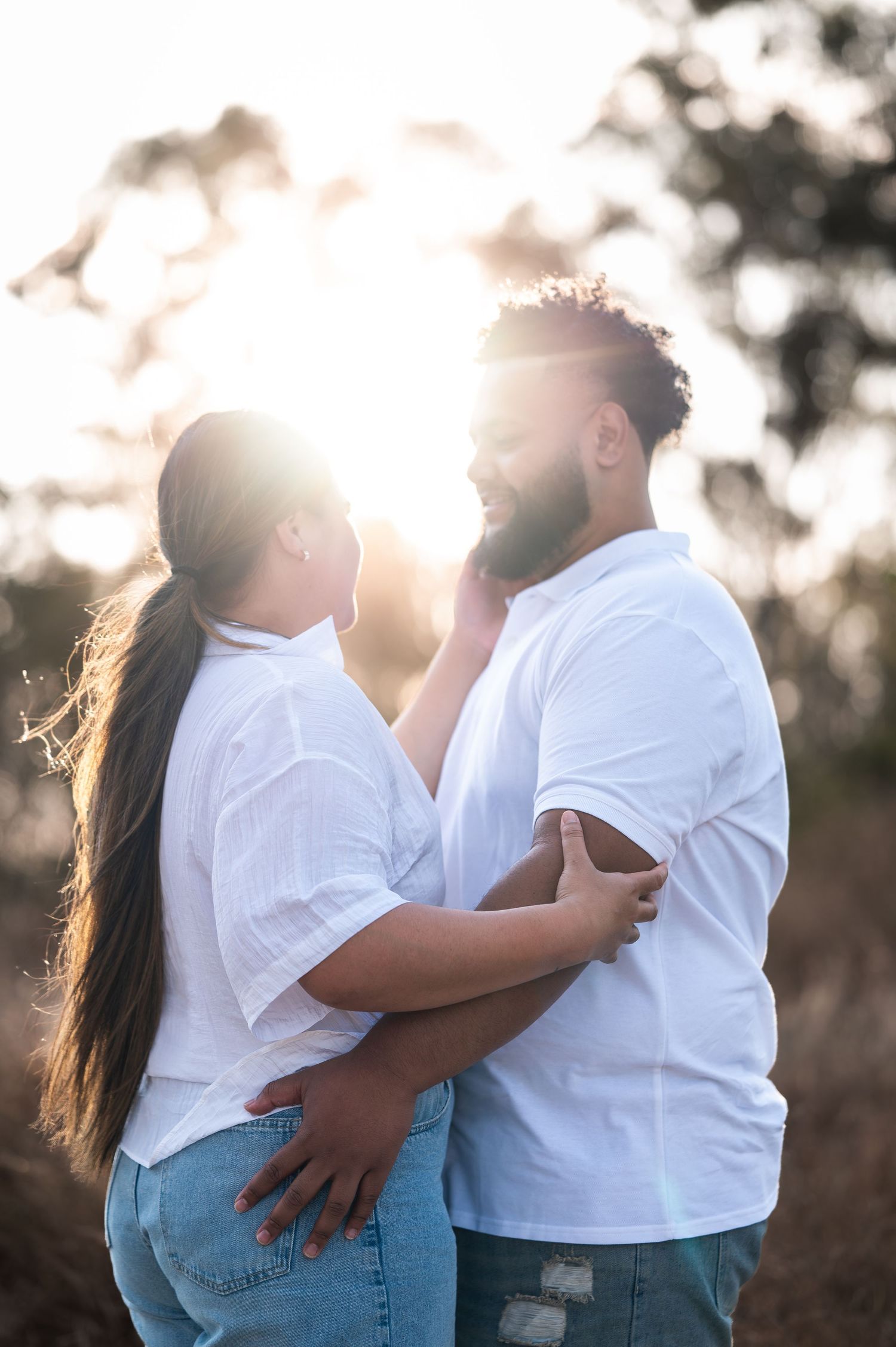 Couple in matching white shirts and jeans embracing against golden sunlit backdrop.