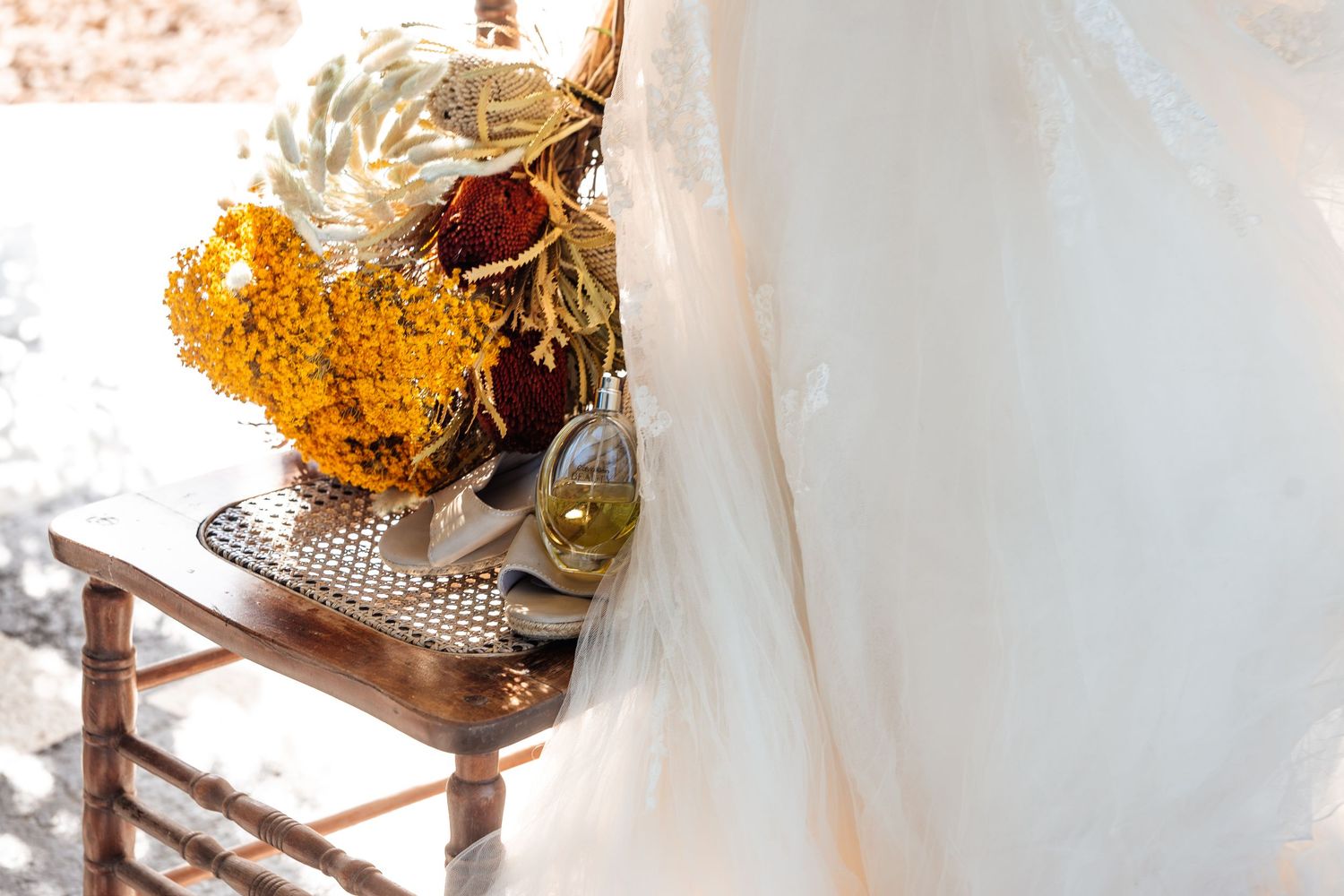 Wedding bouquet and accessories arranged on a vintage wooden chair in natural light.