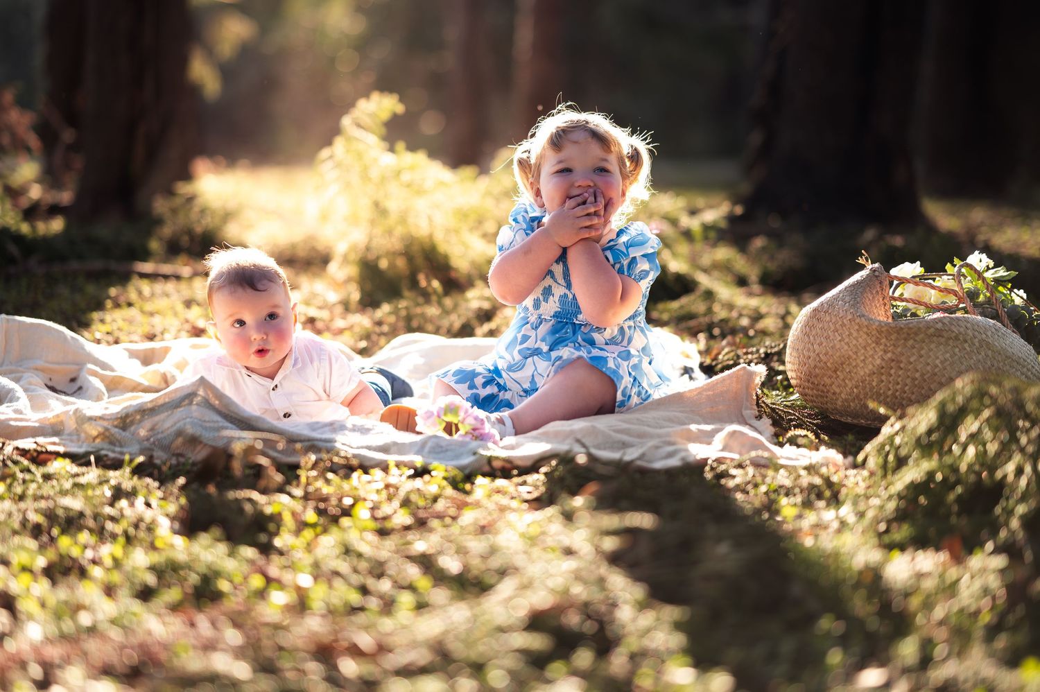 Family relaxing on a blanket during an outdoor photo session in dappled sunlight.