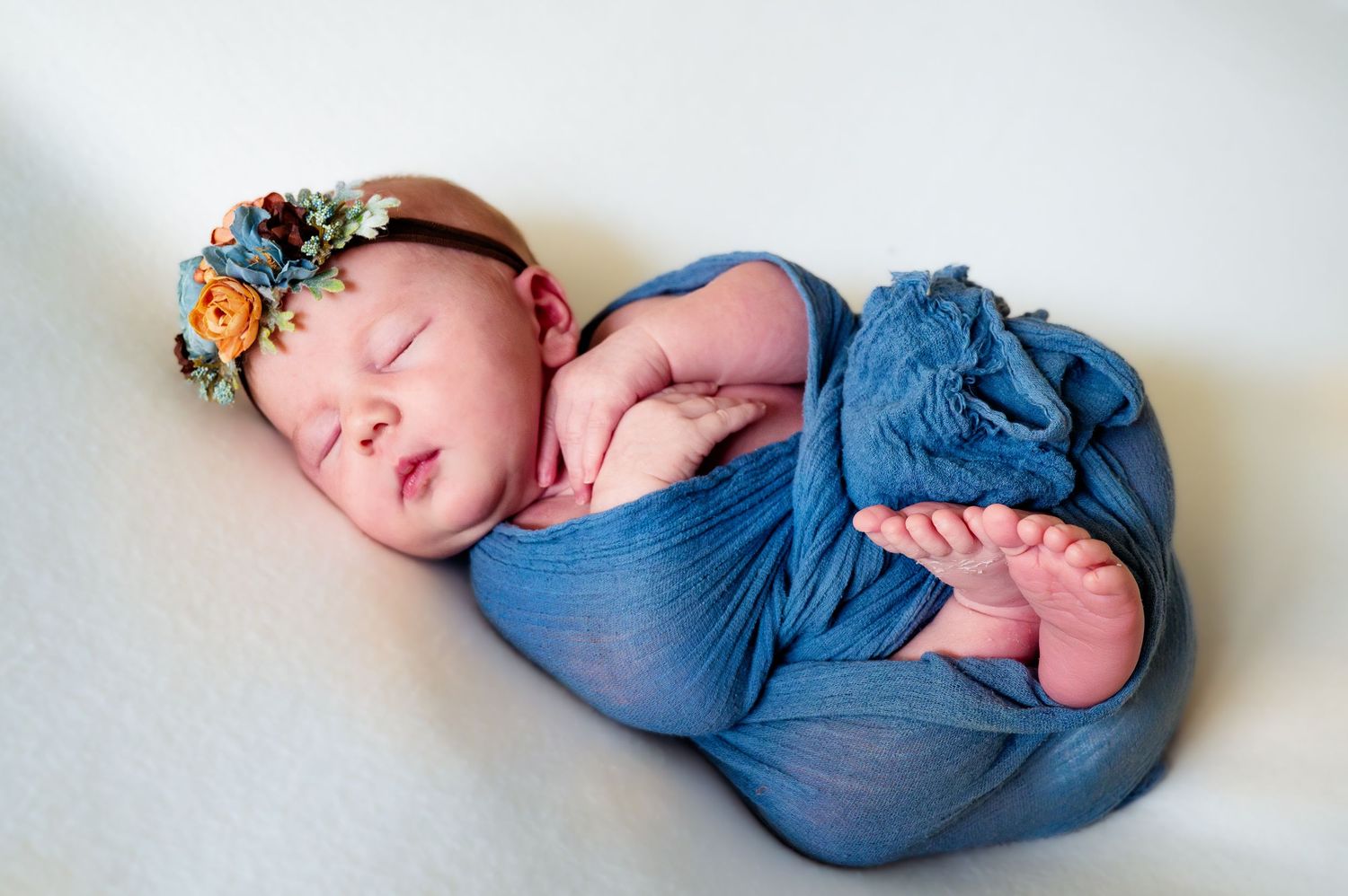 Peaceful newborn wrapped in blue fabric on white background.
