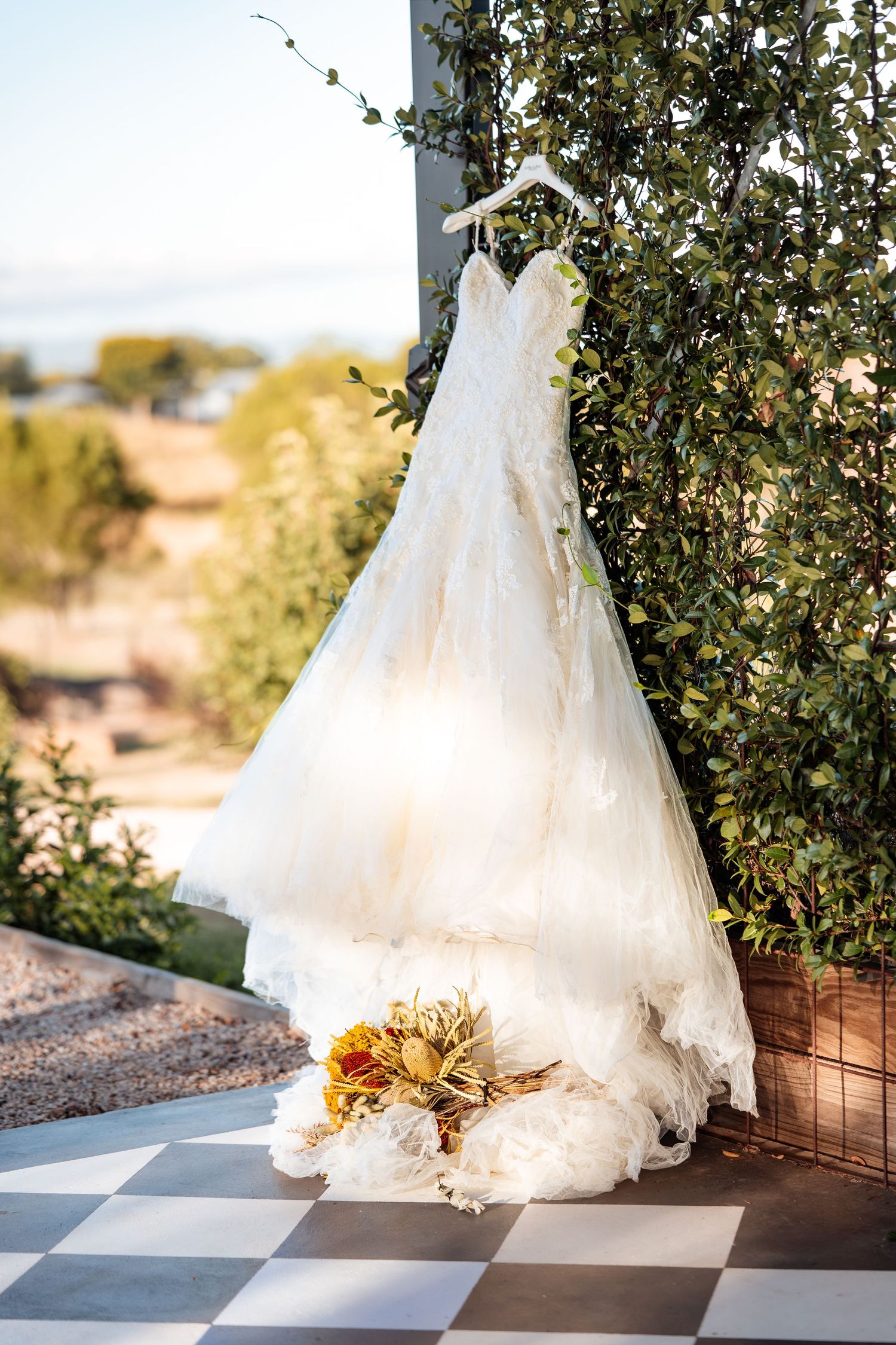 A white wedding dress hanging outdoors with sunflowers against green foliage.
