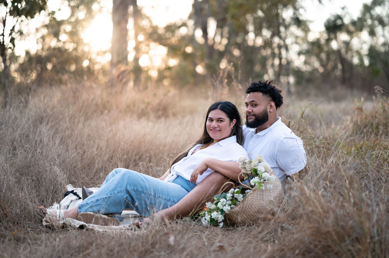Couple lounging on blanket during outdoor photo session in natural setting.