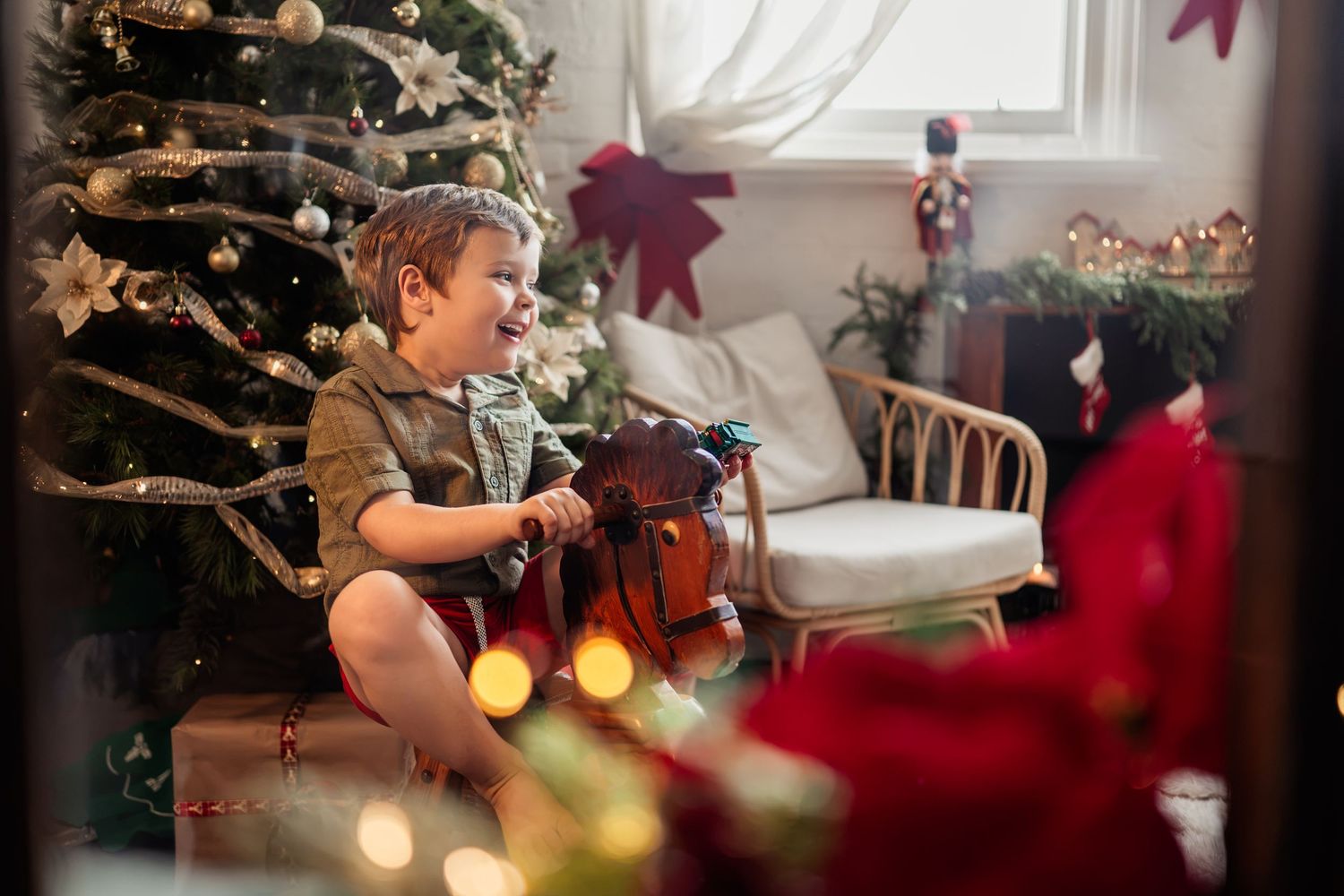 Toddler boy happily opening Christmas gifts near a decorated tree with festive holiday decorations.