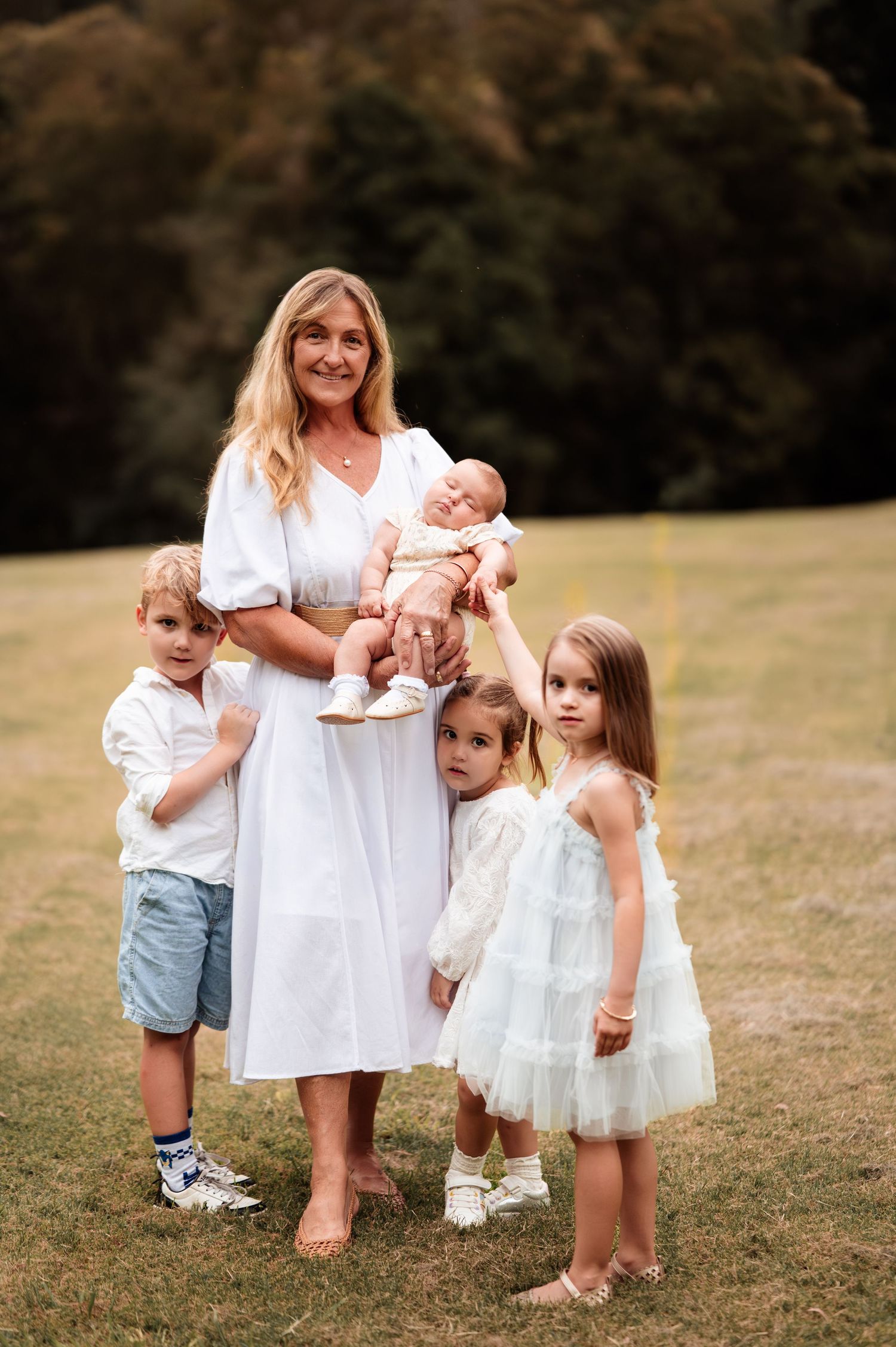 Family group portrait on grass with children in white and pastel clothing.
