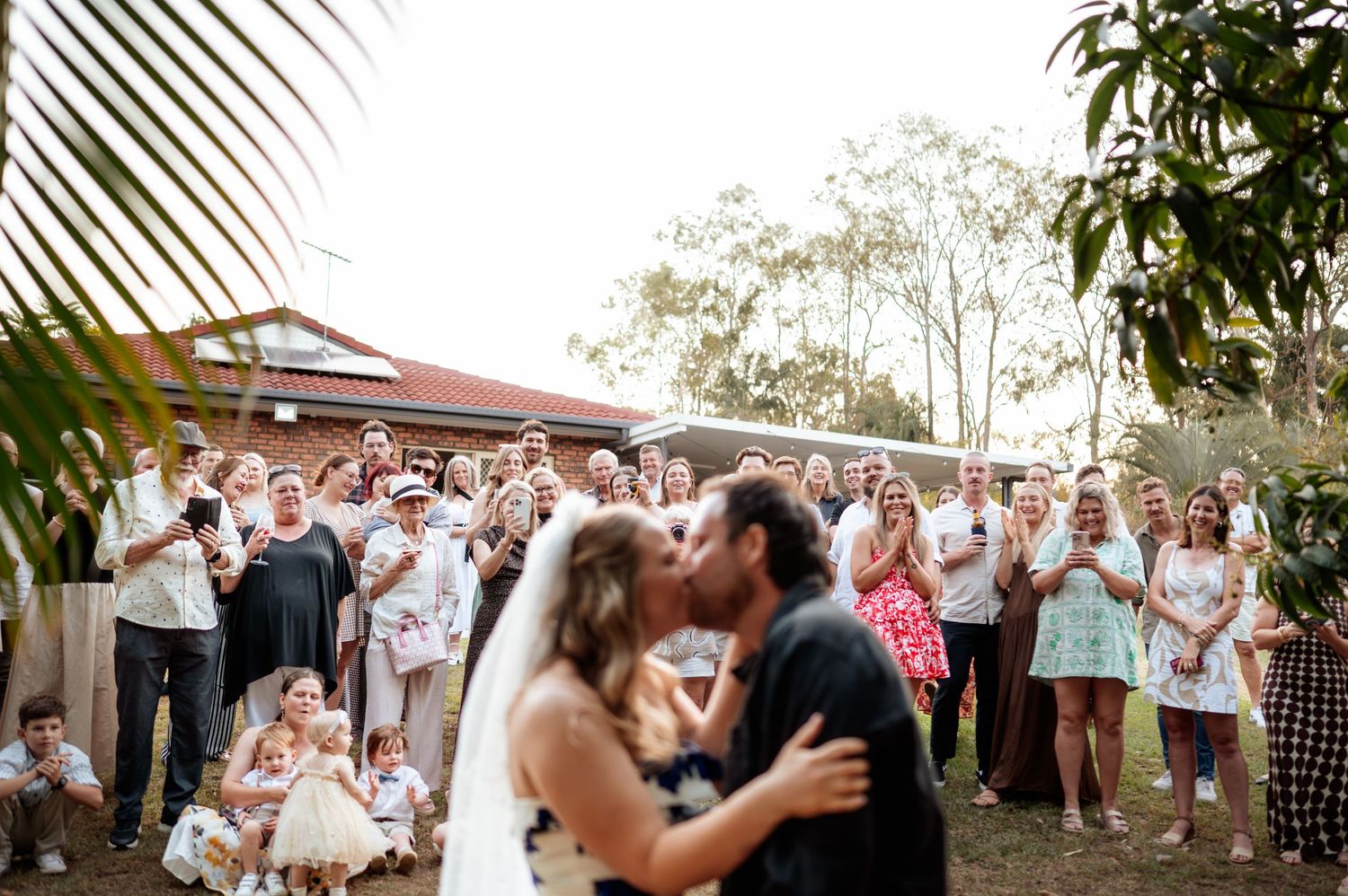 A wedding couple shares their first dance surrounded by applauding guests at sunset.
