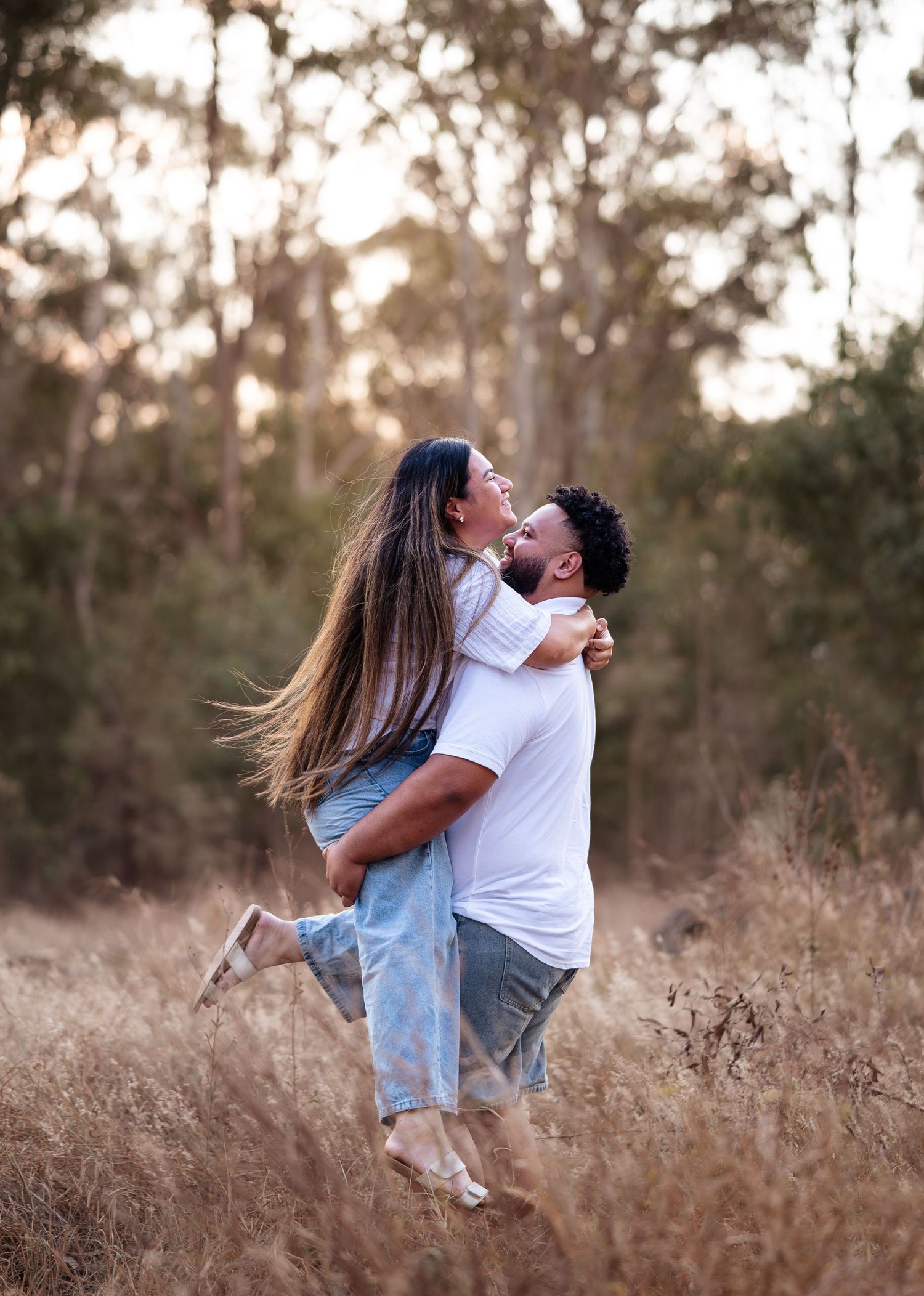 Romantic couple embraces in a sunlit field of tall grass during golden hour.