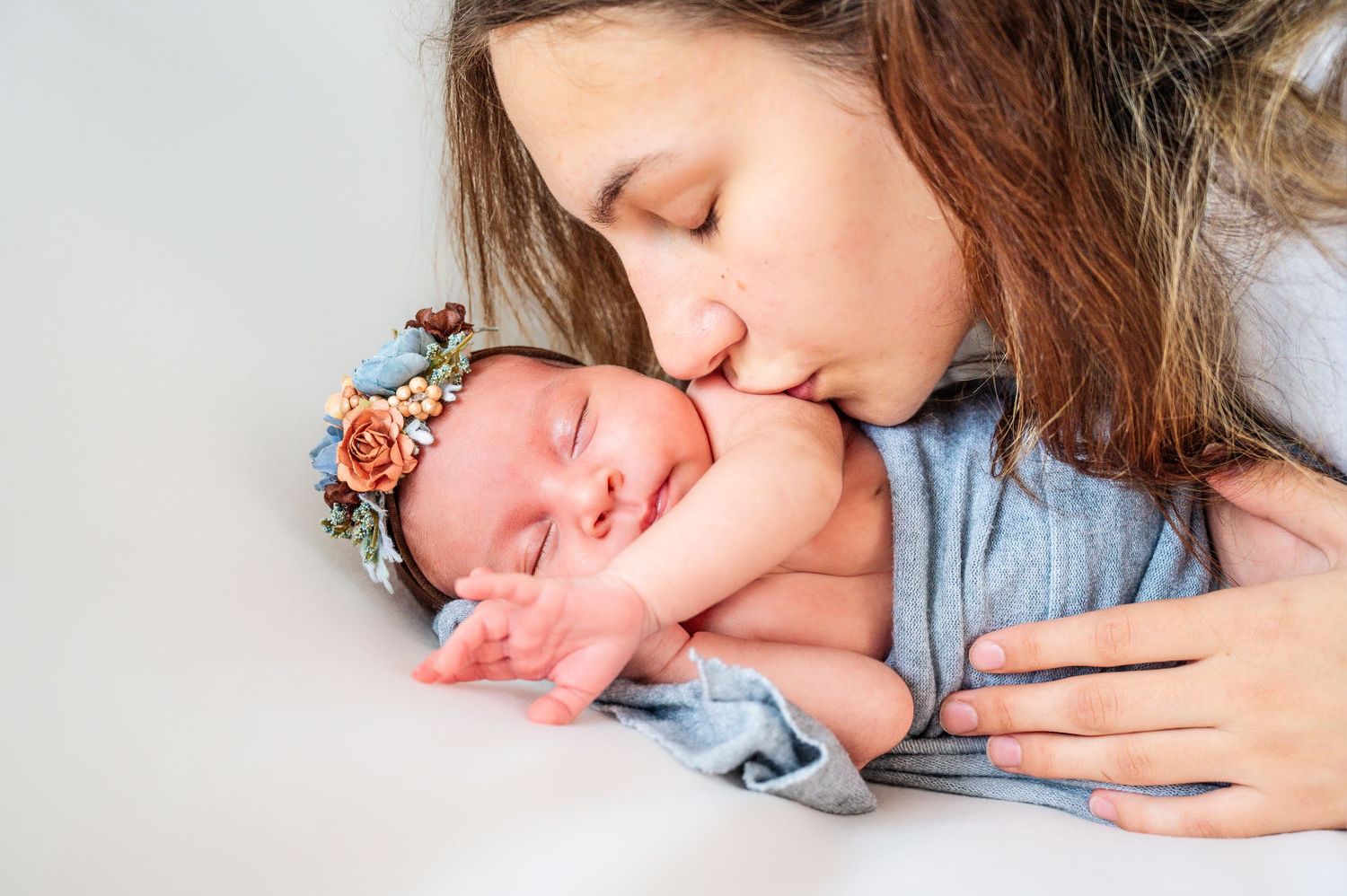Tender moments captured between mother and sleeping newborn in soft lighting.