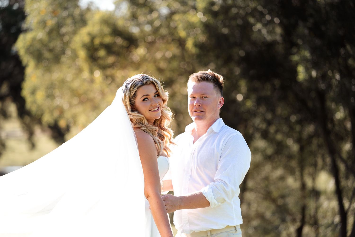 Bride and groom portrait outdoors with flowing veil in natural bushland setting.