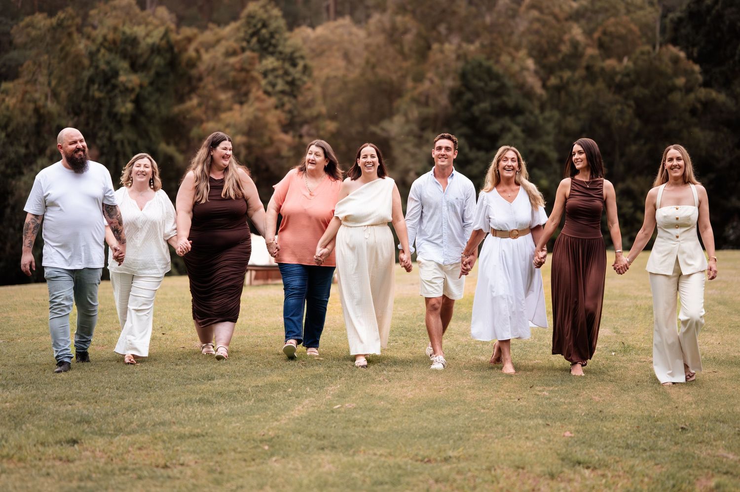 Large family group walking together in white outfits across a grassy field.