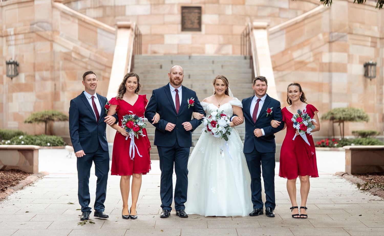 Wedding party of five posing on steps, bridesmaids in red dresses with bouquets.