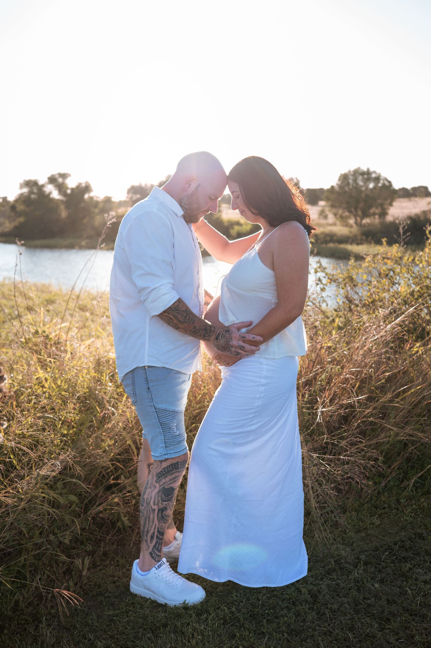 Side view of expecting couple sharing tender moment in field during sunset.
