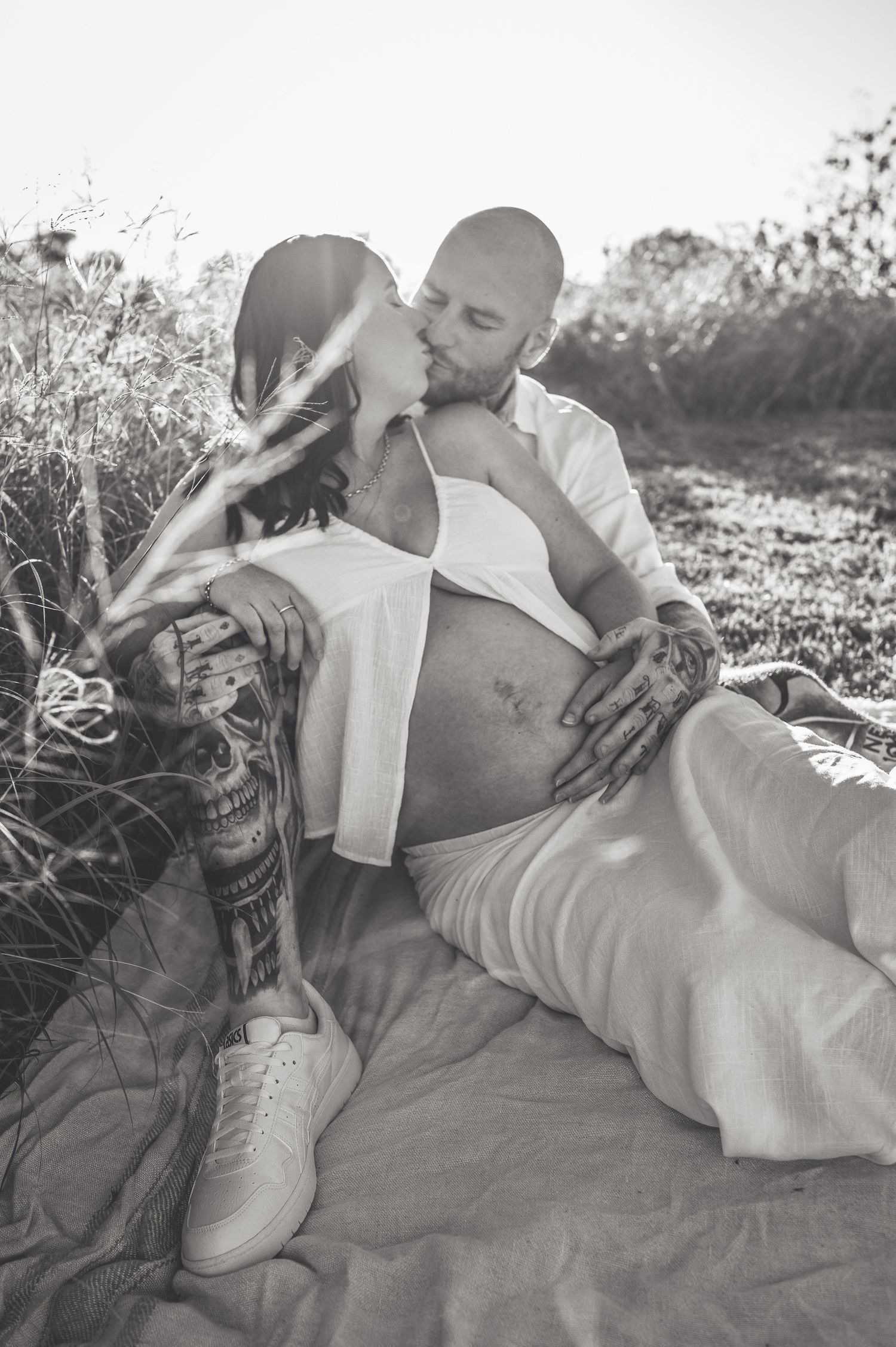 Black and white maternity photos showing couple embracing on ground in natural setting.
