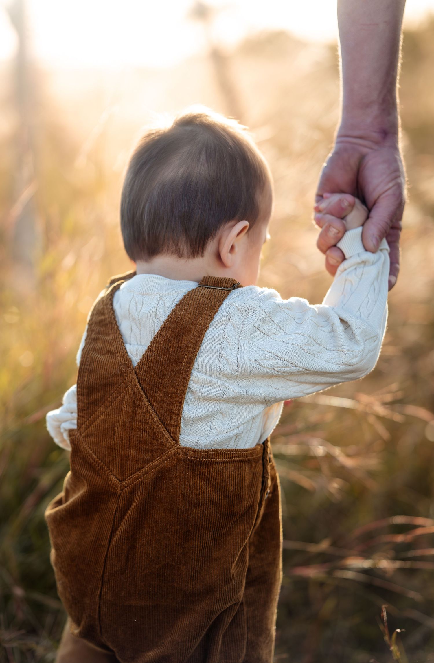 Close-up of a child wearing brown corduroy overalls in golden sunlight.