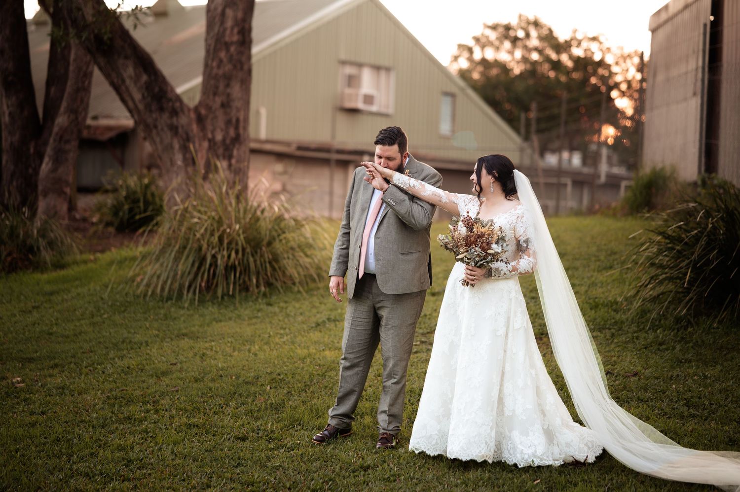 Bride and groom share a tender first look moment on green lawn at golden hour, bride in lace gown holding bouquet.