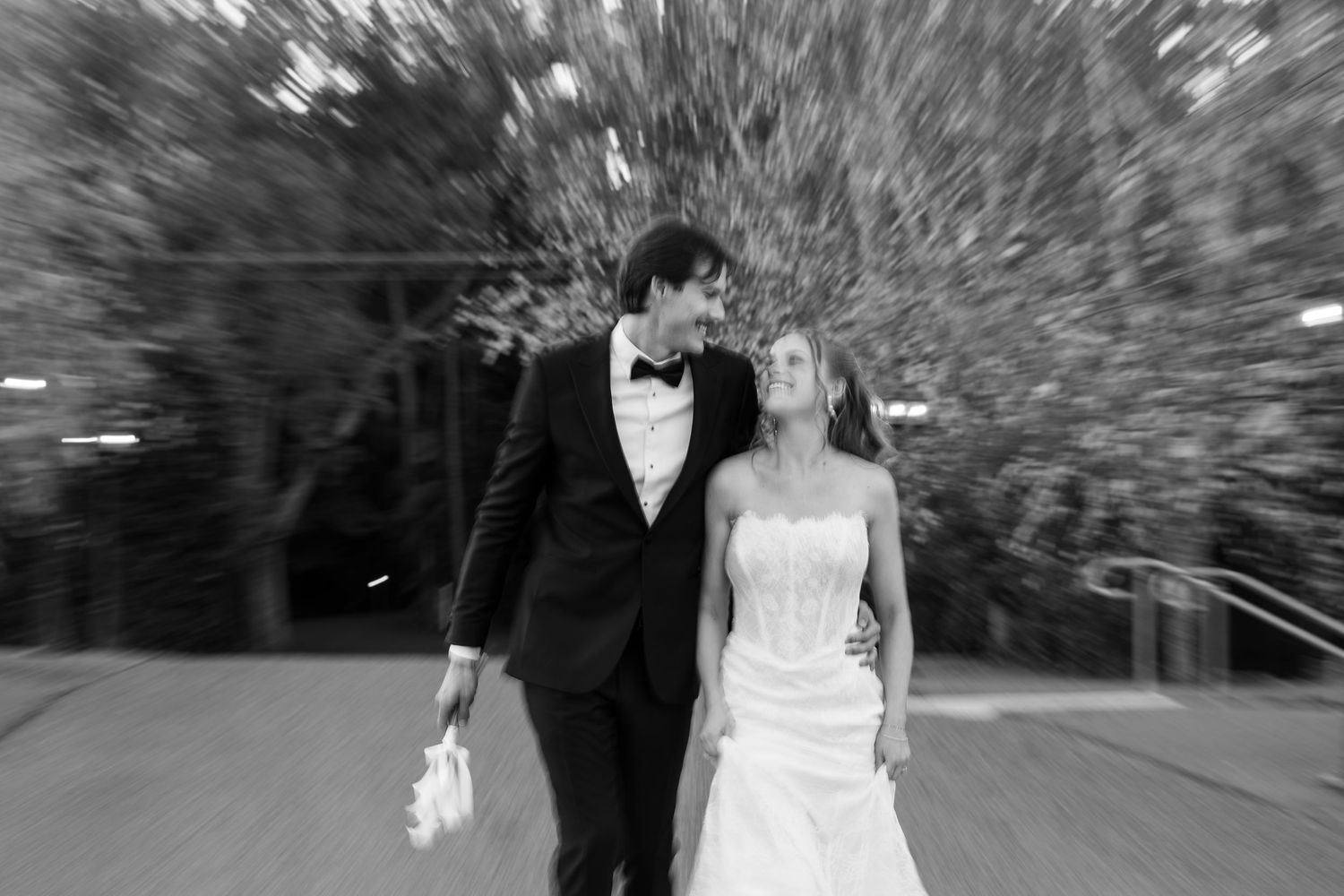 Bride and groom walking together outdoors in black and white wedding photo with motion blur effect.