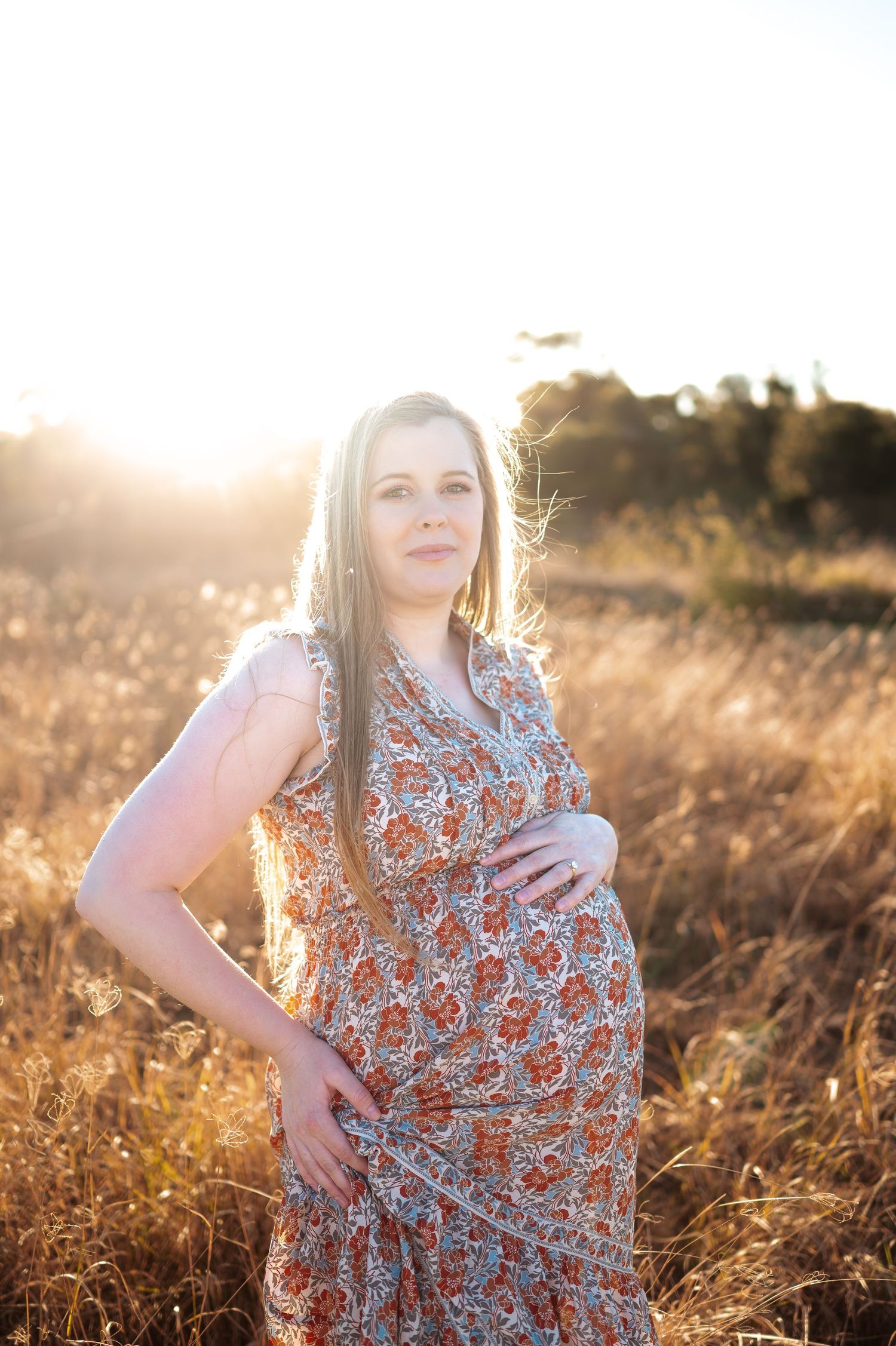 Woman in floral dress poses in golden field during sunset photoshoot.