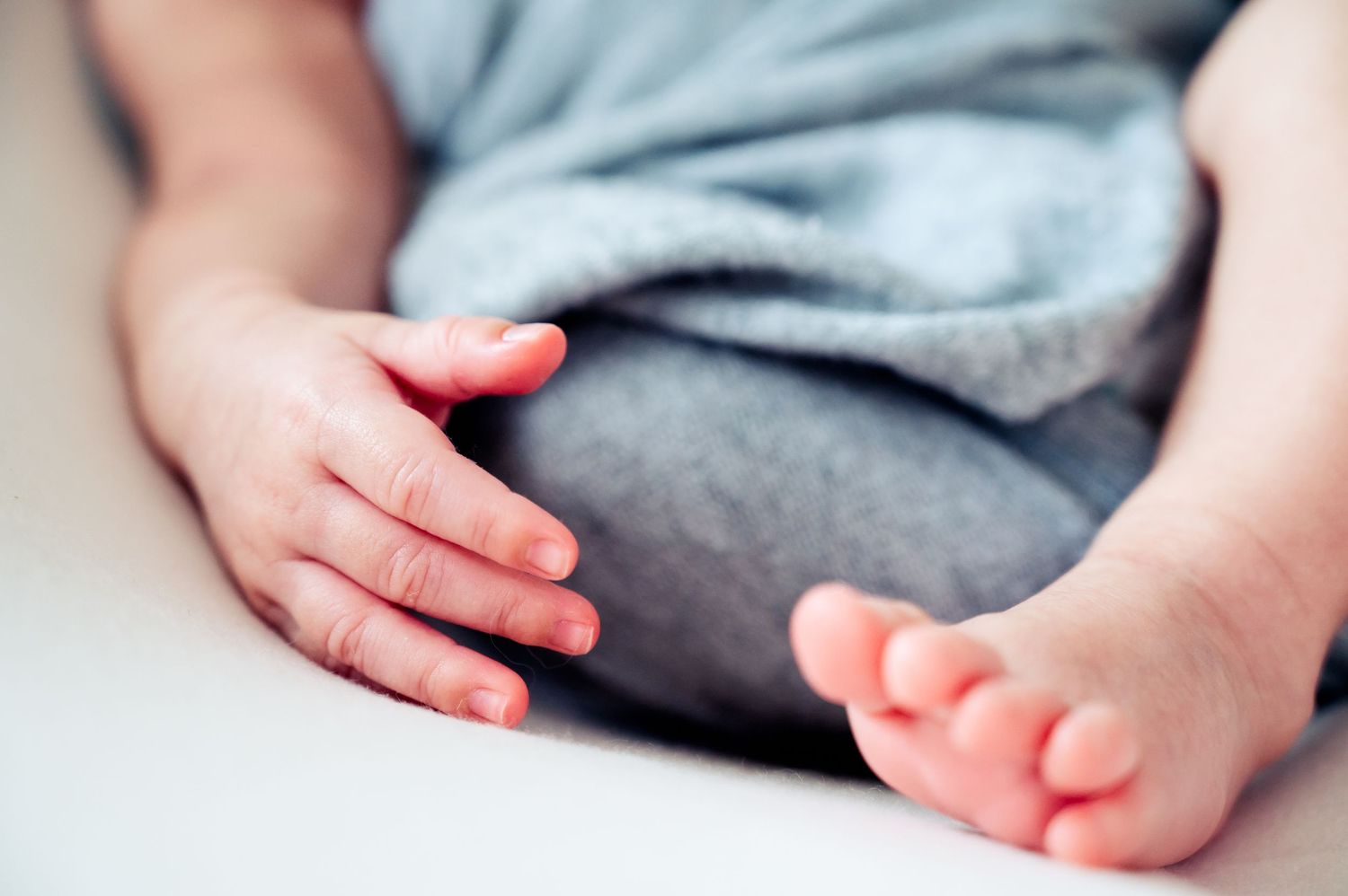 Close-up detail of tiny newborn baby feet wrapped in soft gray blanket.