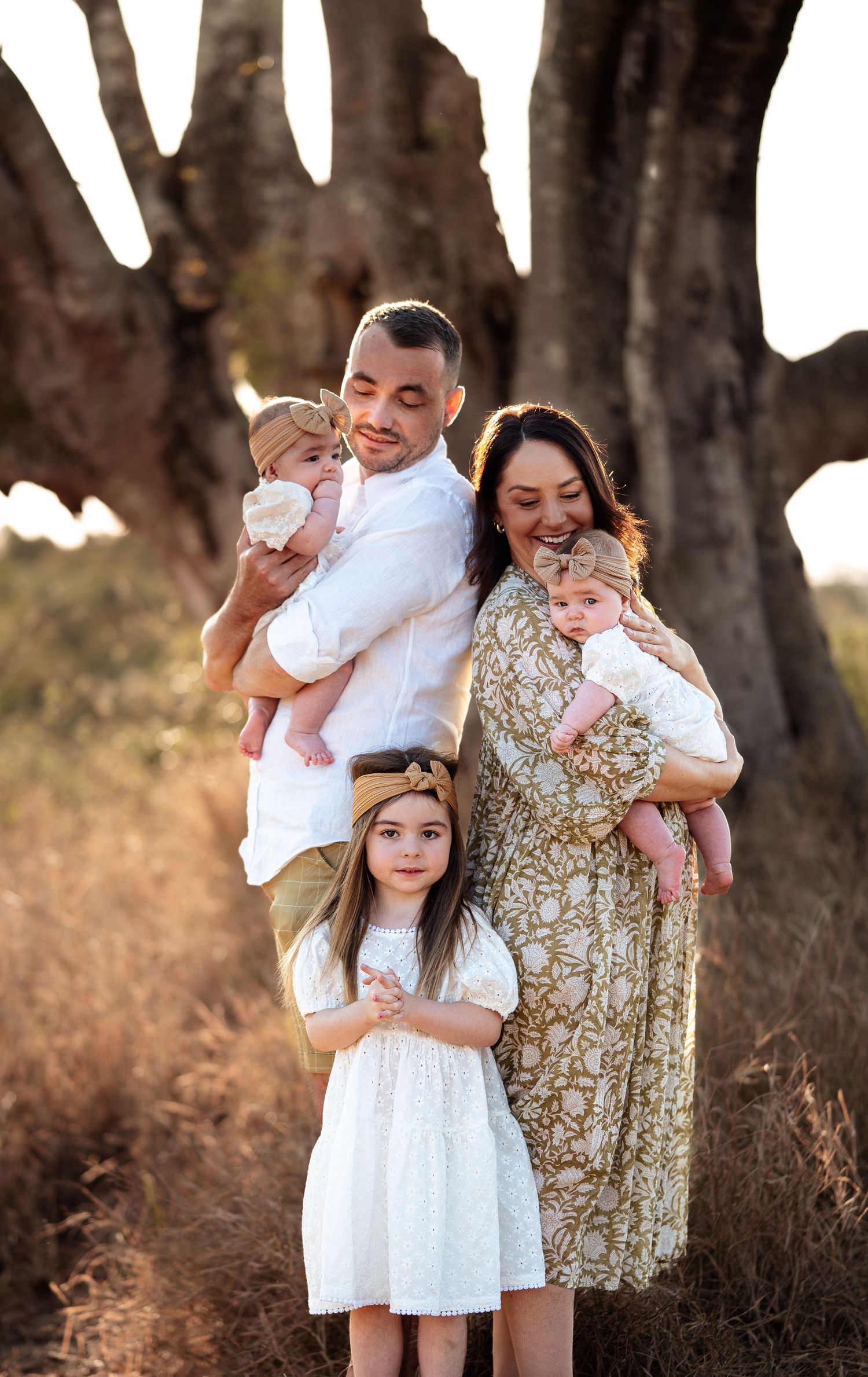 A family photo session in a wooded area with golden sunlight and white and floral outfits.