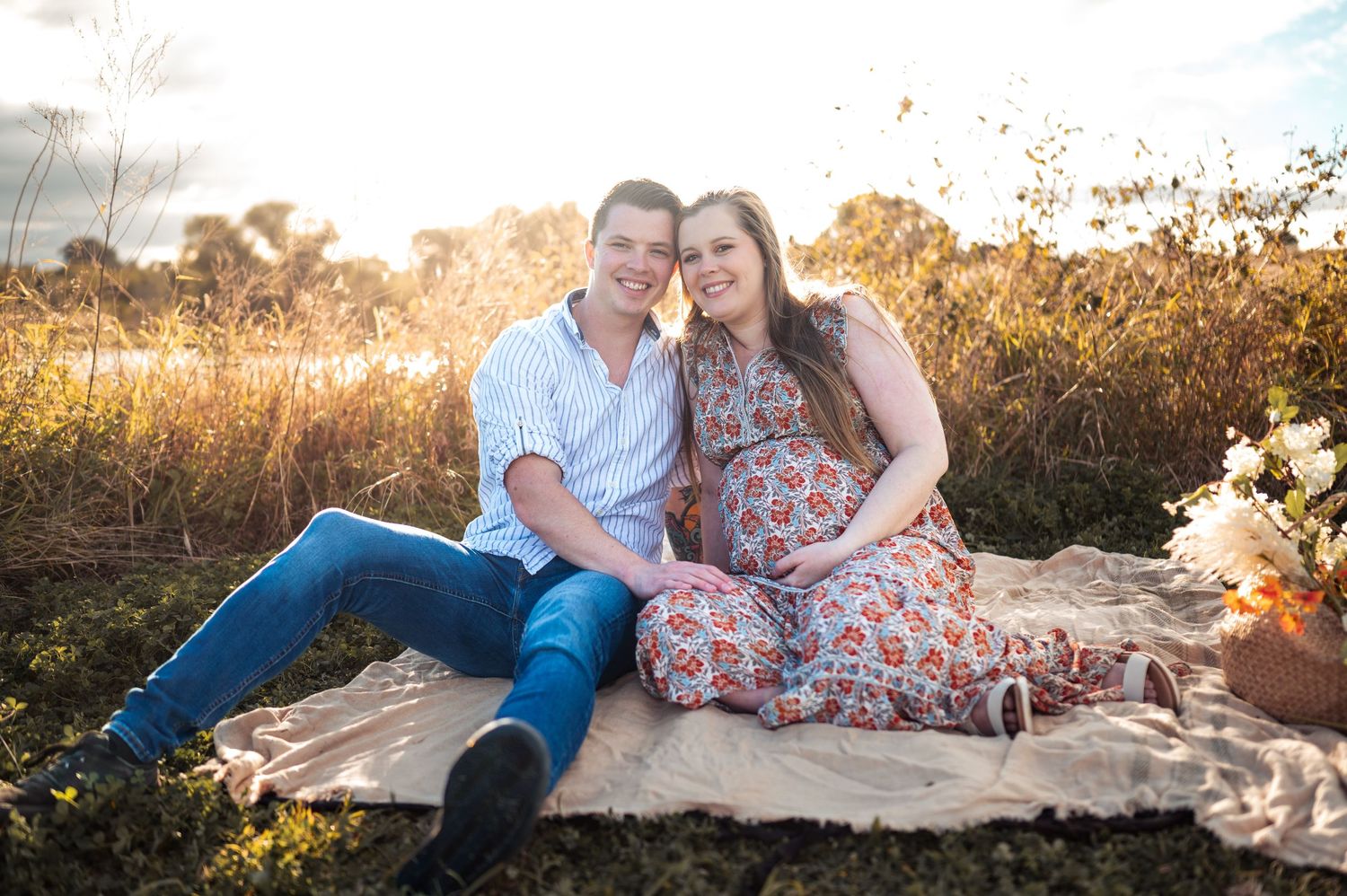 Family poses on blanket during outdoor maternity photoshoot at sunset.
