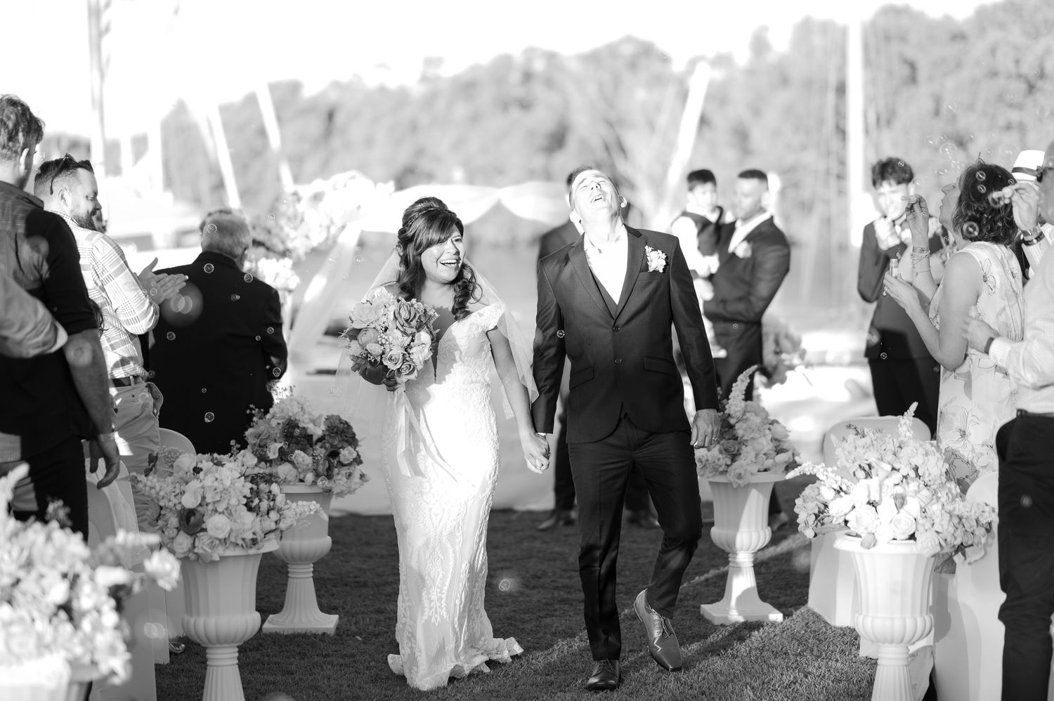 Bride and groom walk down the aisle at outdoor wedding ceremony as guests celebrate with confetti.