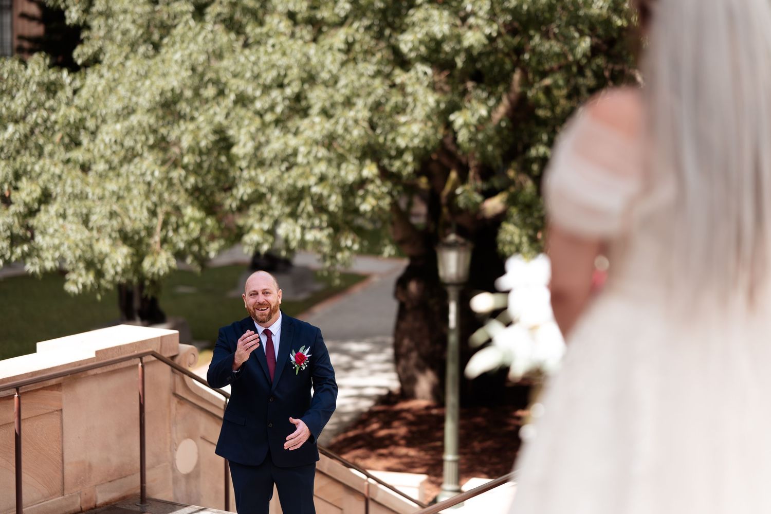 Groom reacting emotionally during a first look moment with his bride outdoors near stone steps.