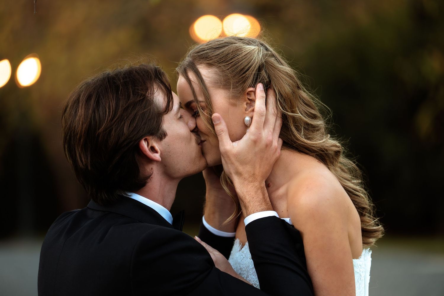 Bride and groom share a romantic kiss at their wedding reception with bokeh lights in the background.