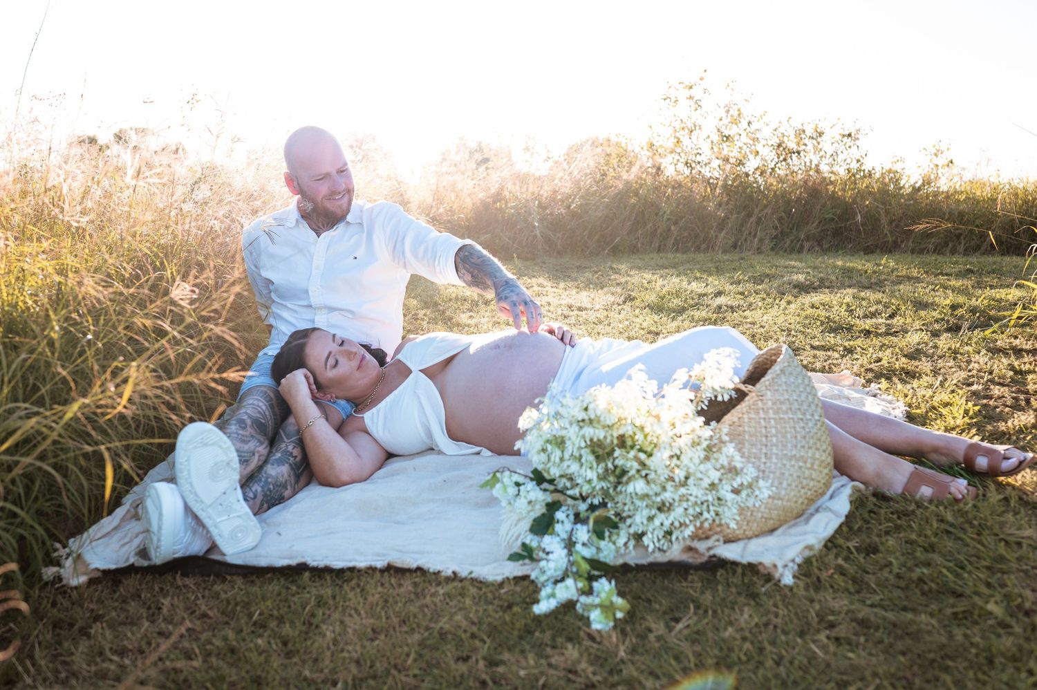 Couple relaxing on blanket during outdoor maternity photography session at golden hour.