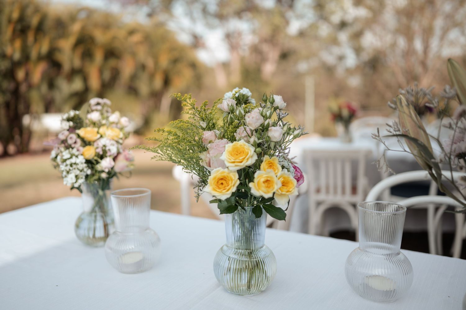 Table decorations featuring mason jars with yellow and white flowers at outdoor reception.