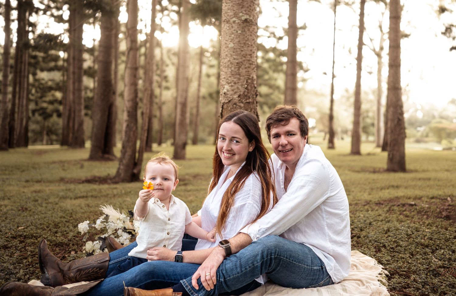 Family relaxing together on grass in a wooded park during golden hour.