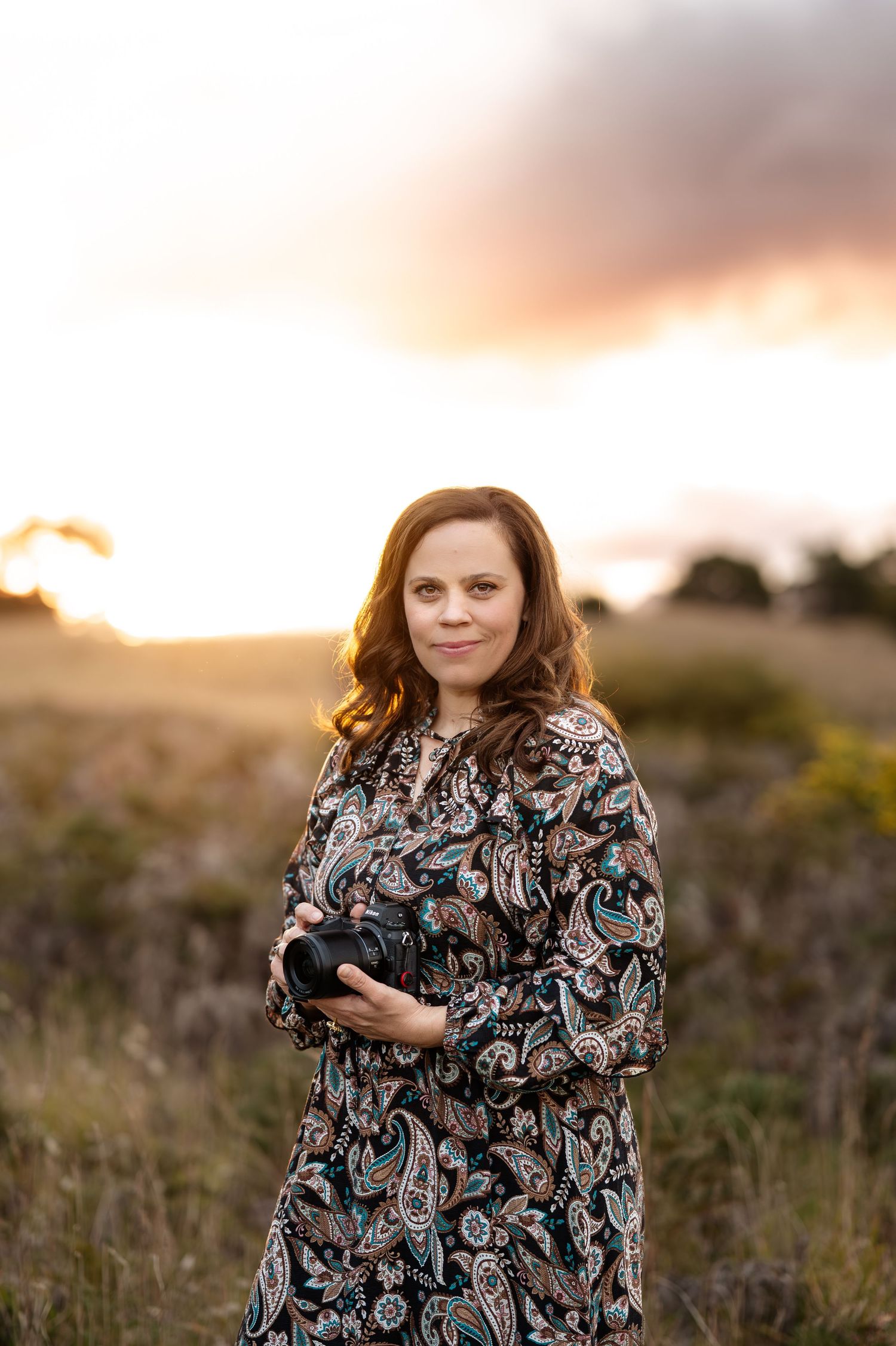 Woman in floral dress poses during sunset in a natural outdoor setting.