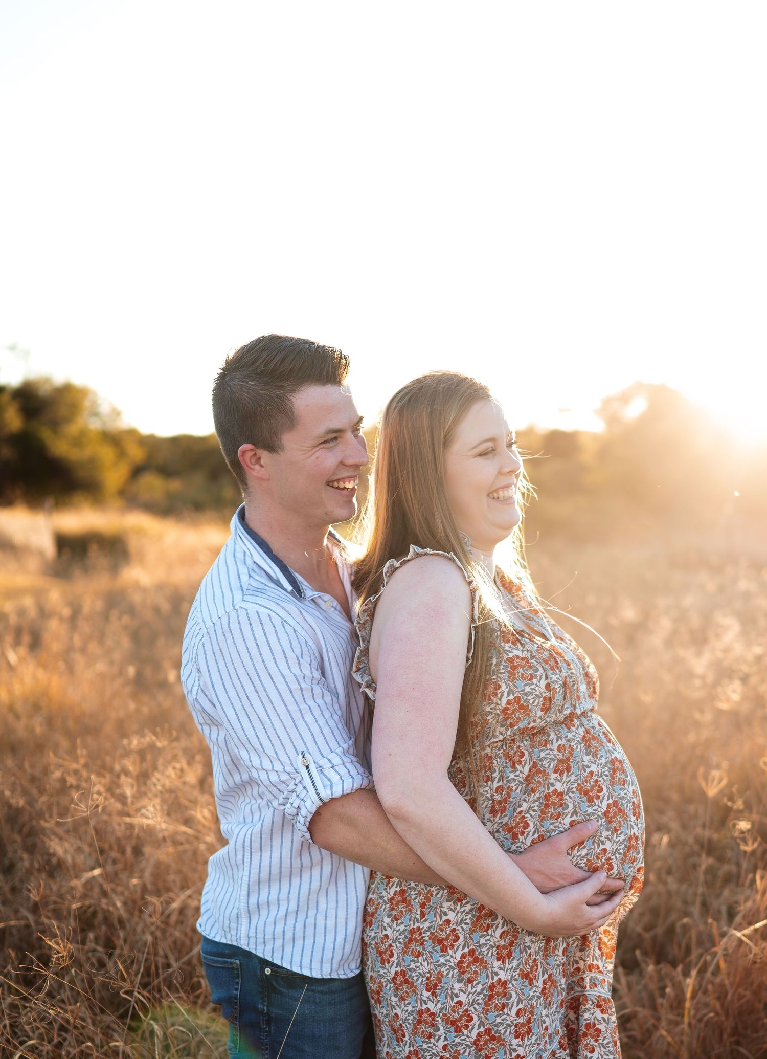 Tender moment between couple in floral dress and striped shirt during golden hour photography session.