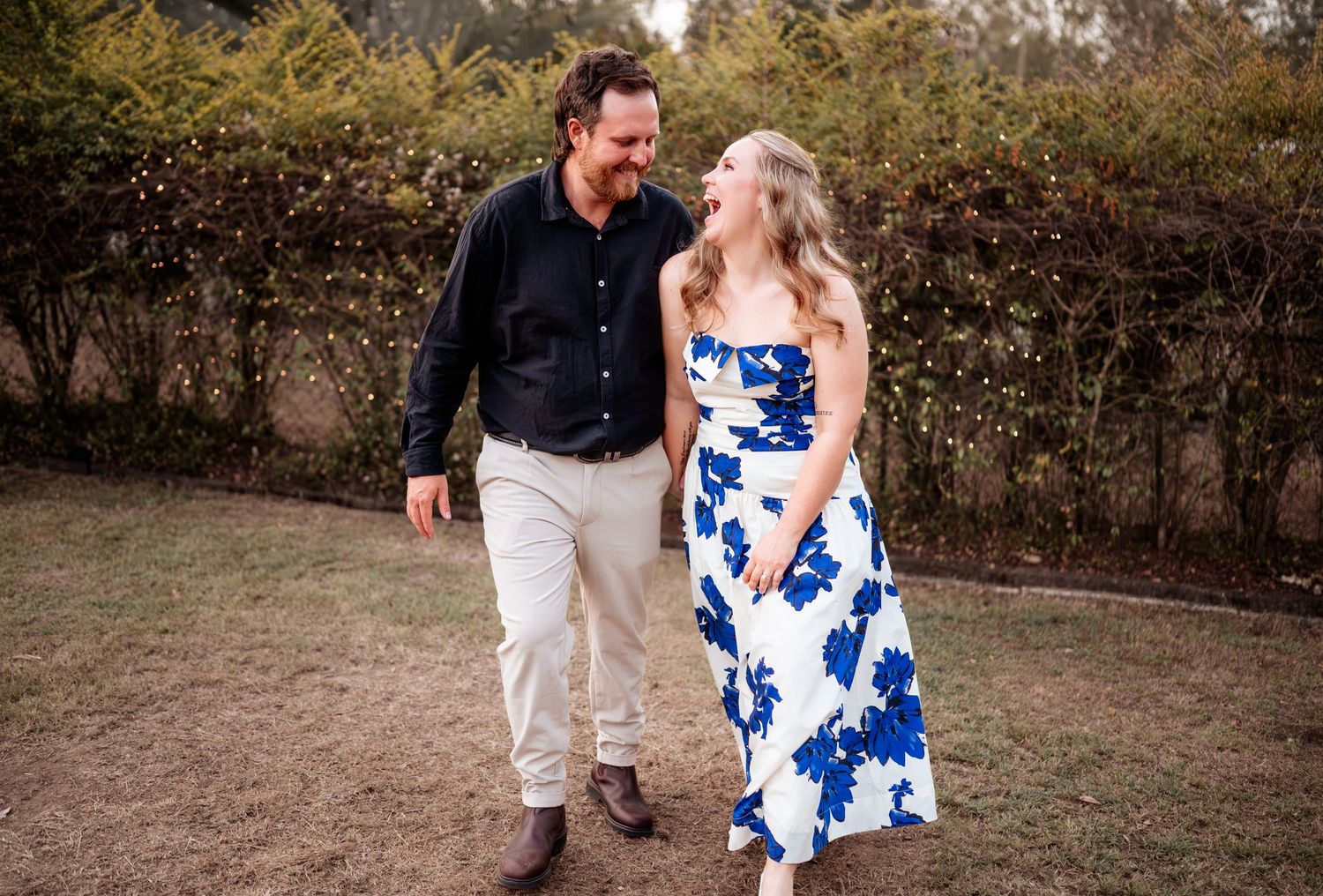 A couple dances together on a dirt path surrounded by greenery at an outdoor event.