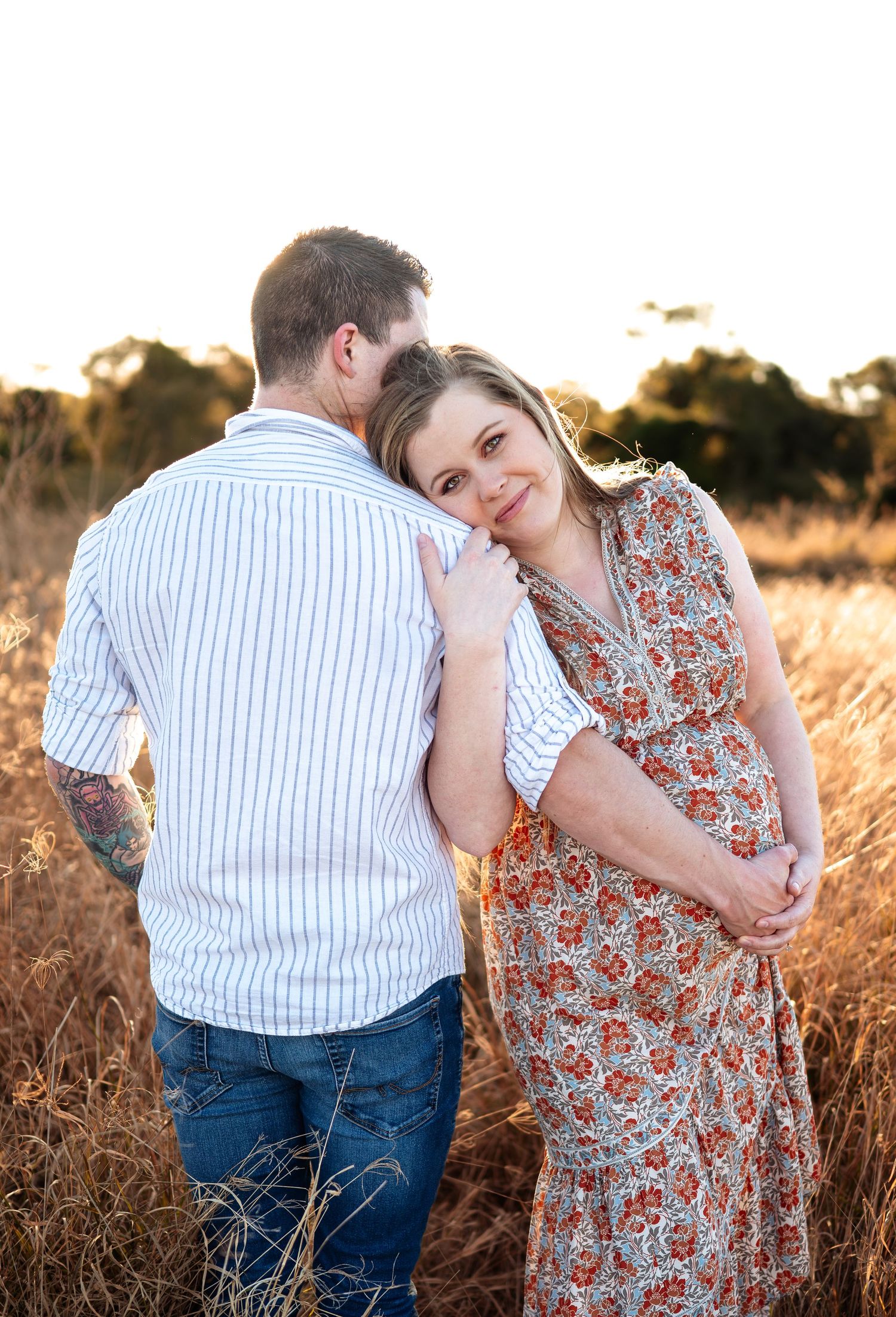 Intimate family moment captured in warm evening light among tall grass and wildflowers.