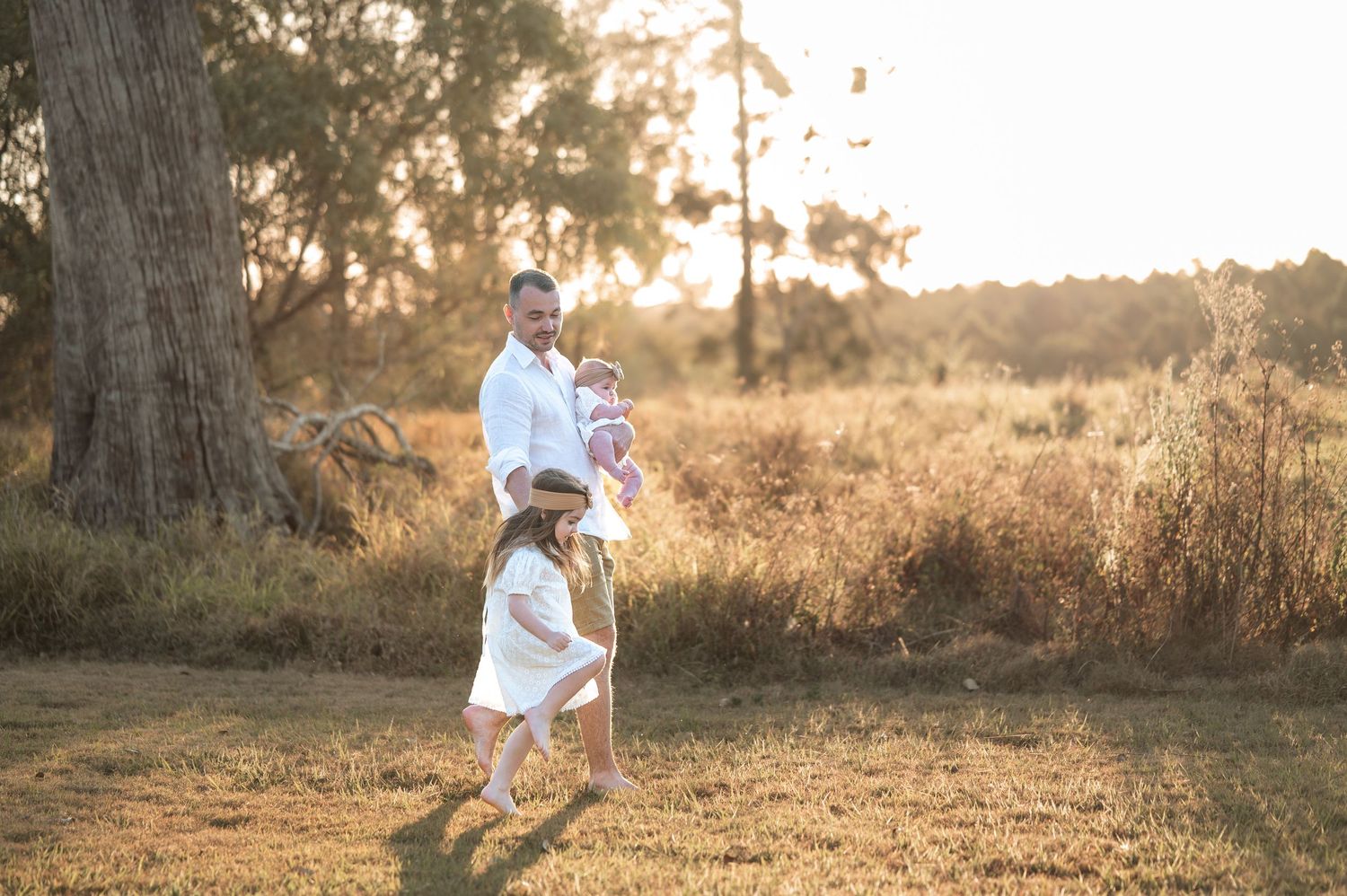 Family playing and running through a grassy field at sunset with trees in background.