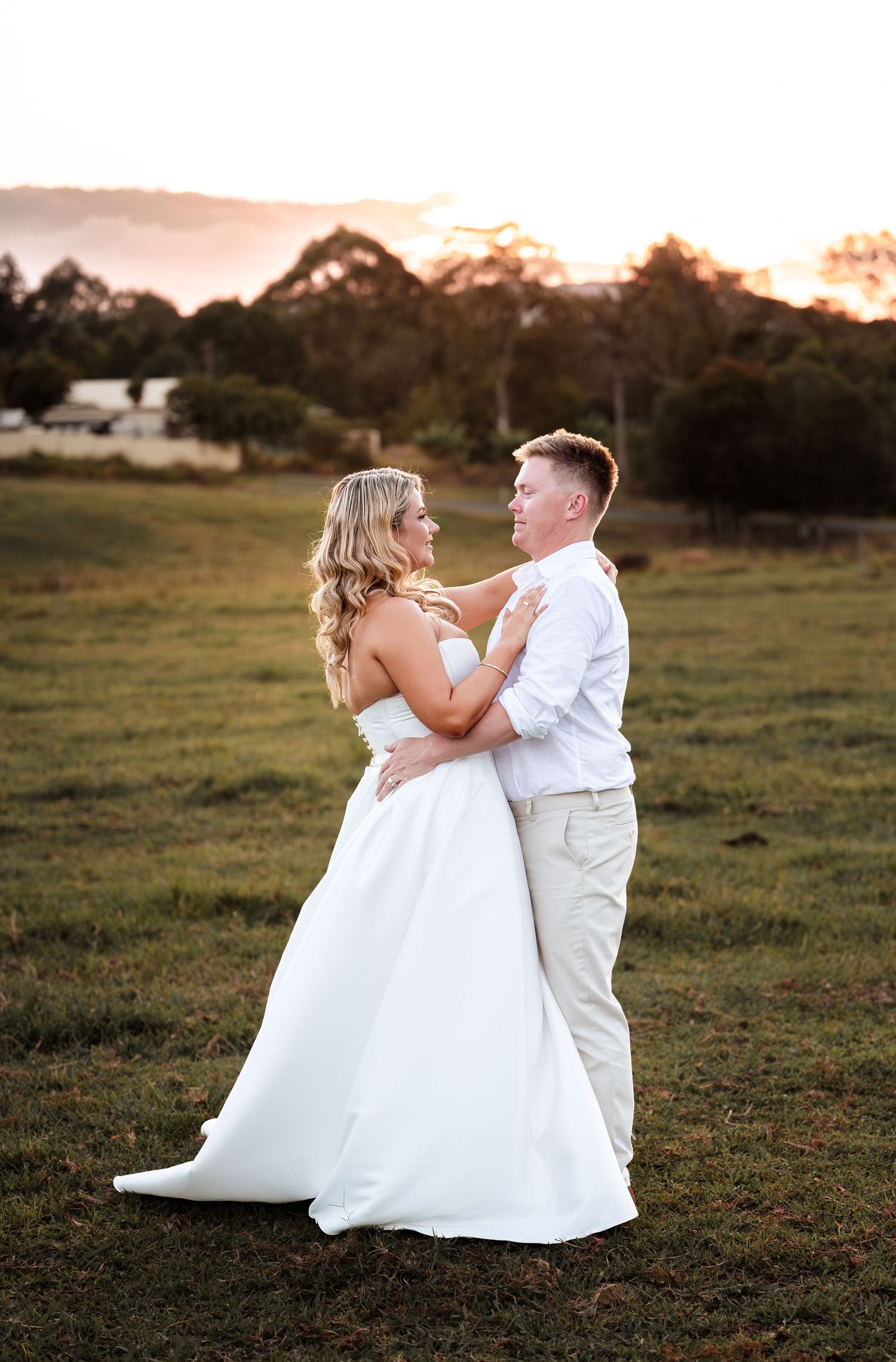 Bride and groom dance in an open field at sunset with mountains and trees in the background.