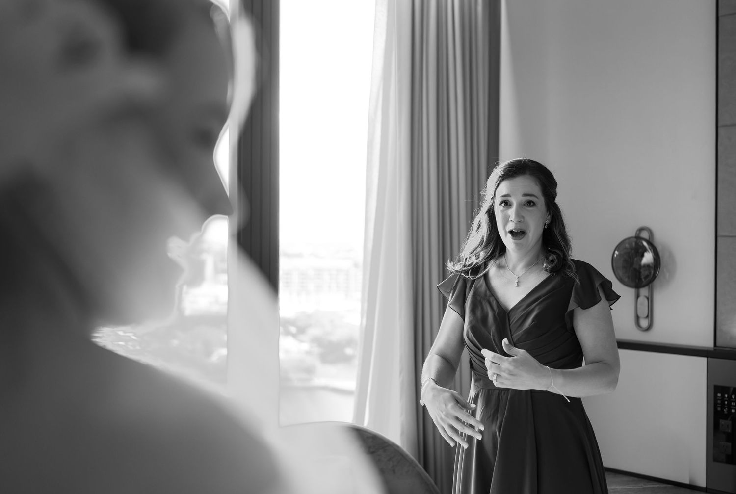 Black and white photo of a surprised bridesmaid reacting with open mouth in an elegant hotel room.