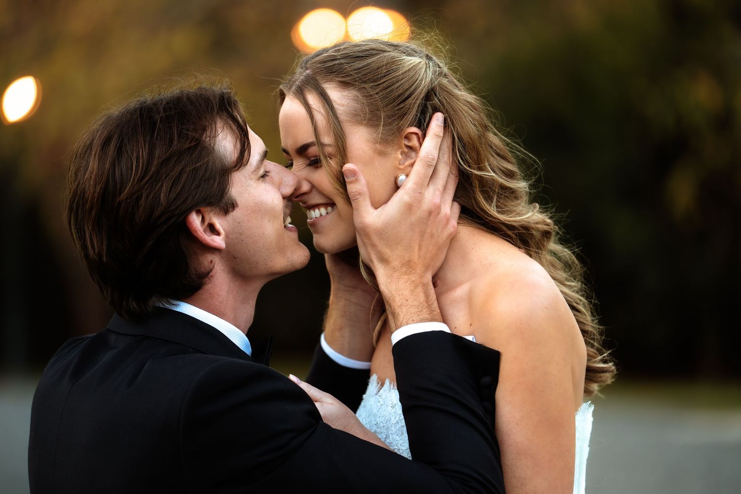 Romantic couple sharing an intimate moment outdoors, man in black suit gently touching woman's face as they embrace.
