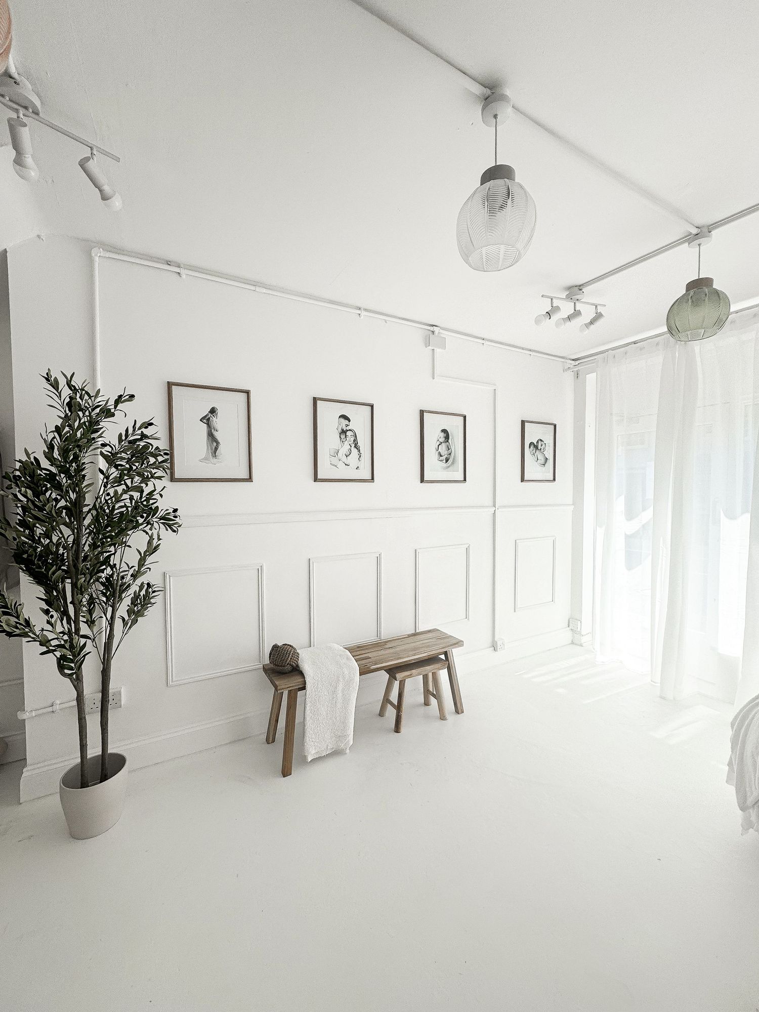 Bright white photography studio with framed wall art, wooden stools, and potted olive tree.