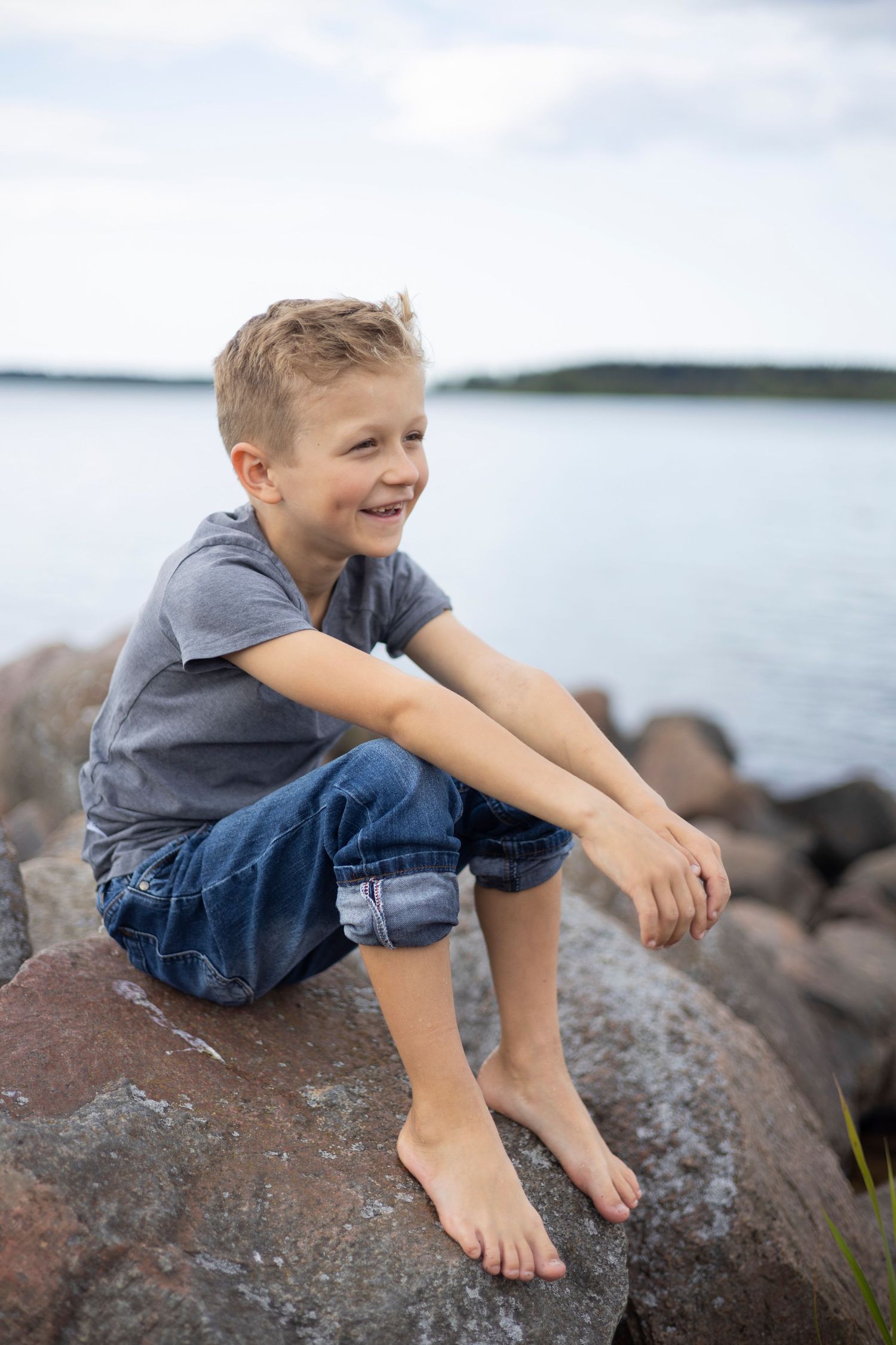 Poika istuu kivellä meren rannalla.