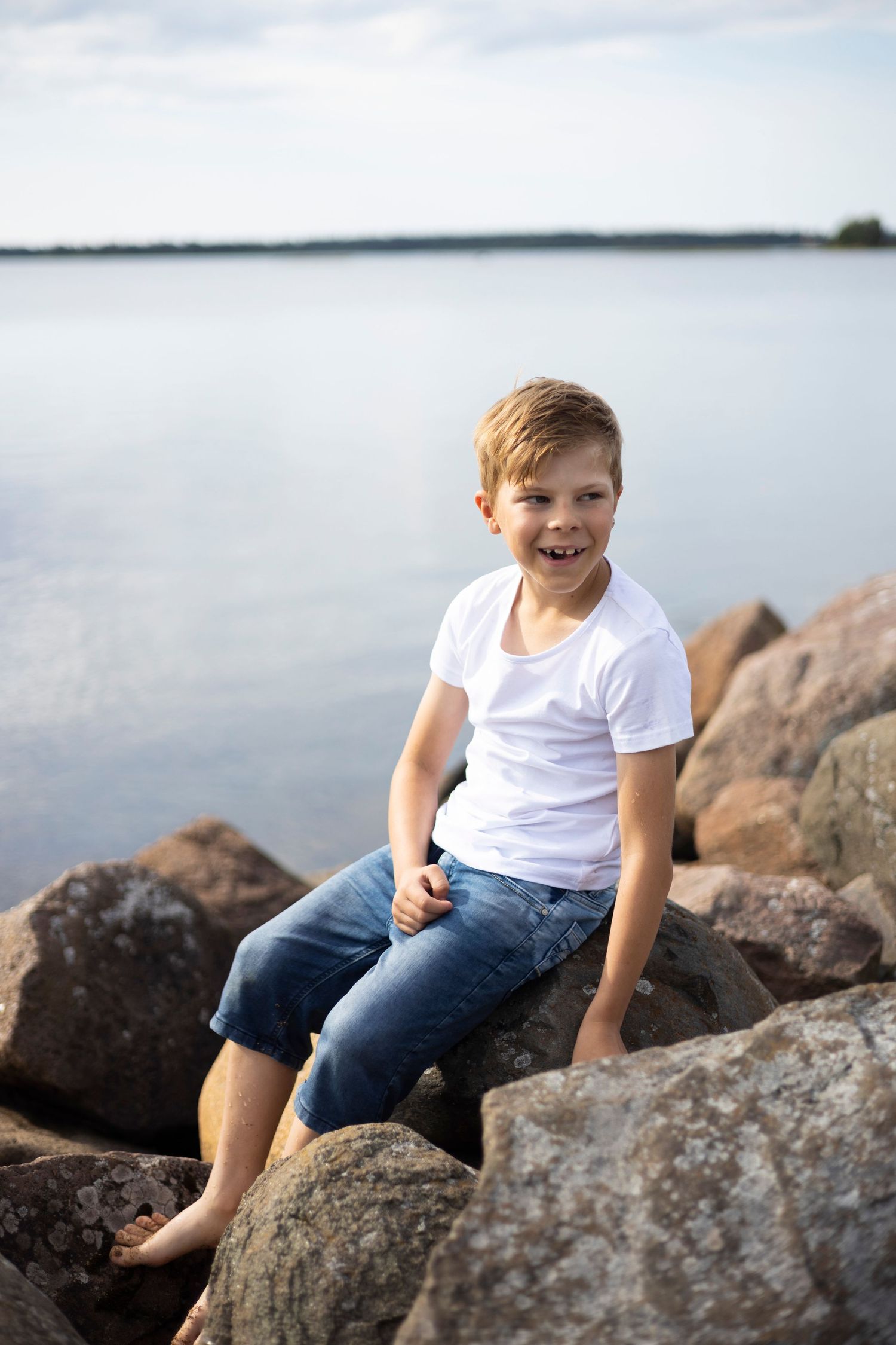Poika nauraa istuessa kivellä meren rannalla Raahessa.