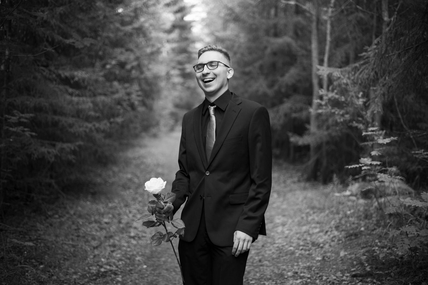 Mies nauraa ruusu kädessä Oulussa metsäisessä miljöössä.
