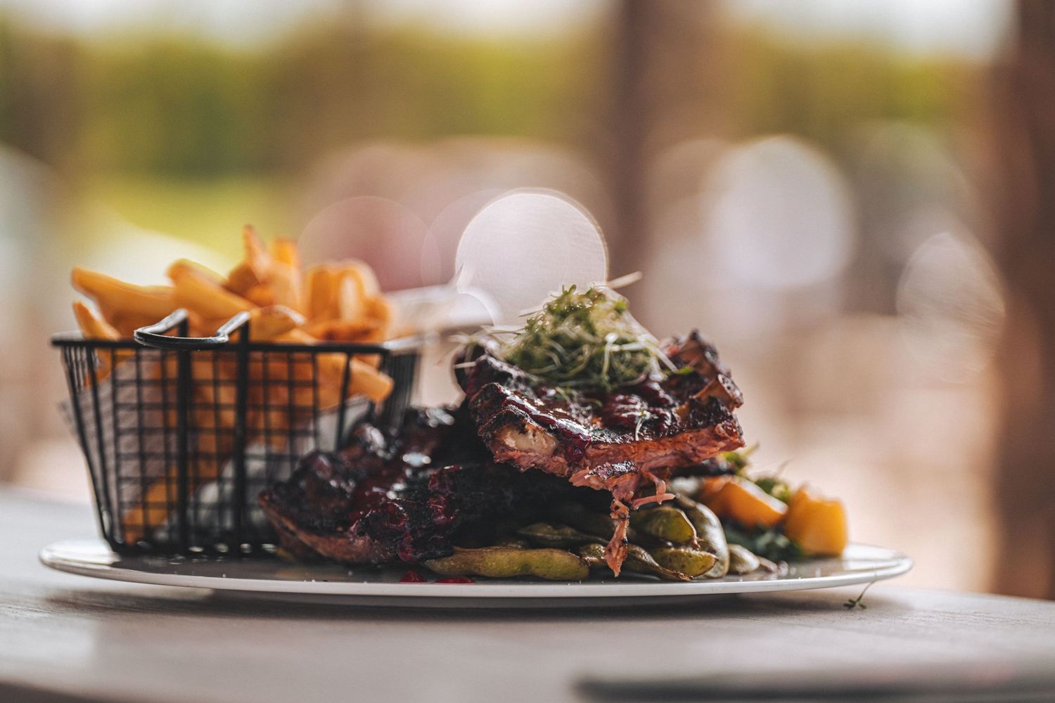 Plate of BBQ ribs served with fries and garnished vegetables at a restaurant.