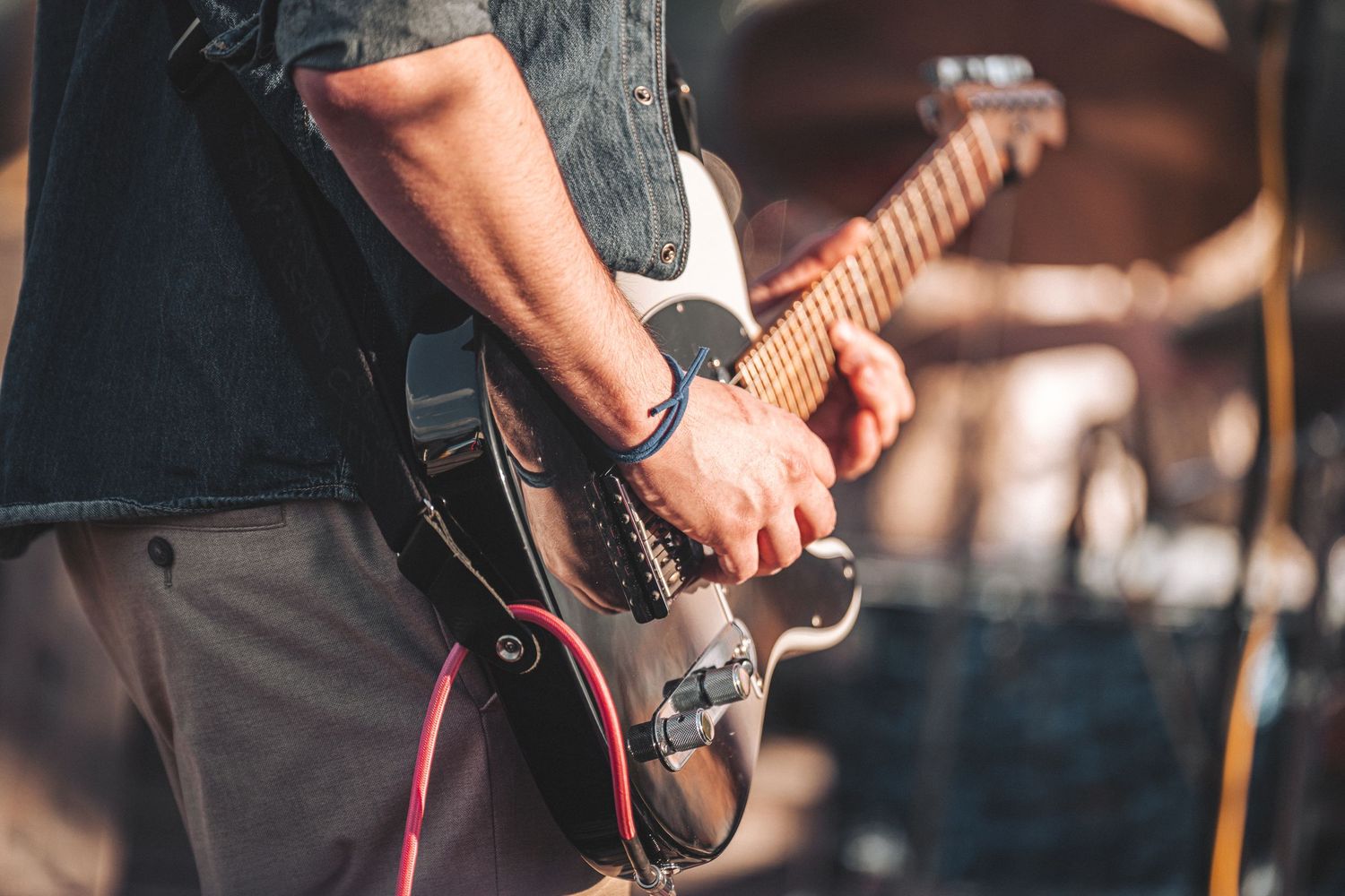 Close-up of musician's hands playing a black electric guitar at an outdoor live event.